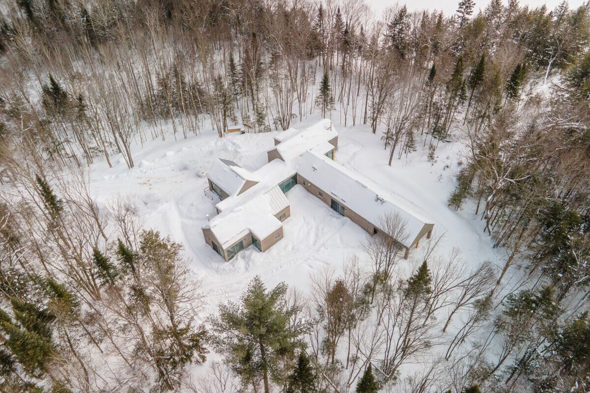 A Quebec mountain house built with cross-laminated timber, featuring gabled volumes and a pinwheel layout that blends into the surrounding landscape.