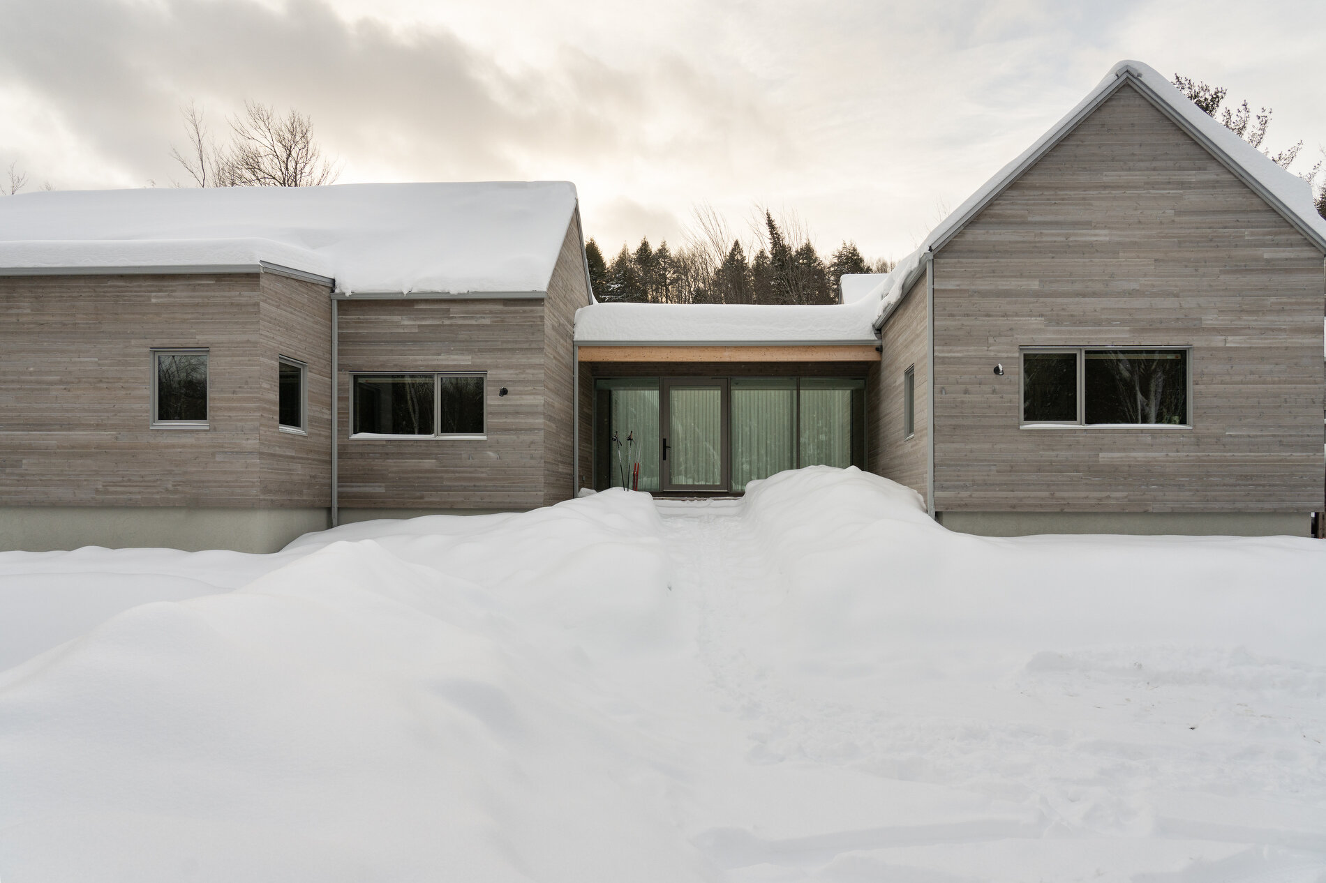 A Quebec mountain house built with cross-laminated timber, featuring gabled volumes and a pinwheel layout that blends into the surrounding landscape.
