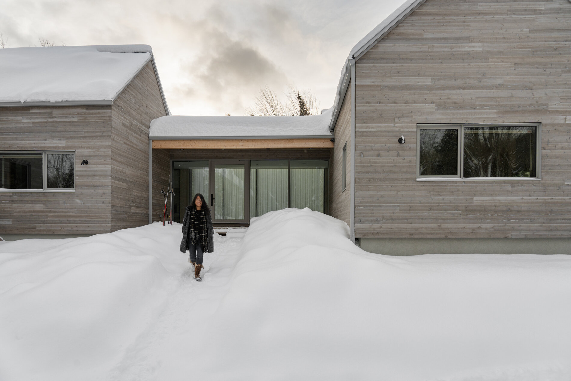 A Quebec mountain house built with cross-laminated timber, featuring gabled volumes and a pinwheel layout that blends into the surrounding landscape.