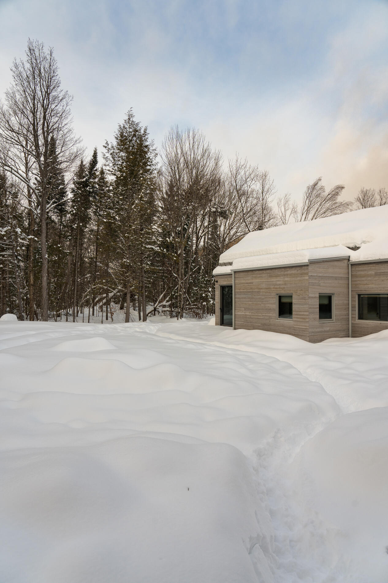 A Quebec mountain house built with cross-laminated timber, featuring gabled volumes and a pinwheel layout that blends into the surrounding landscape.