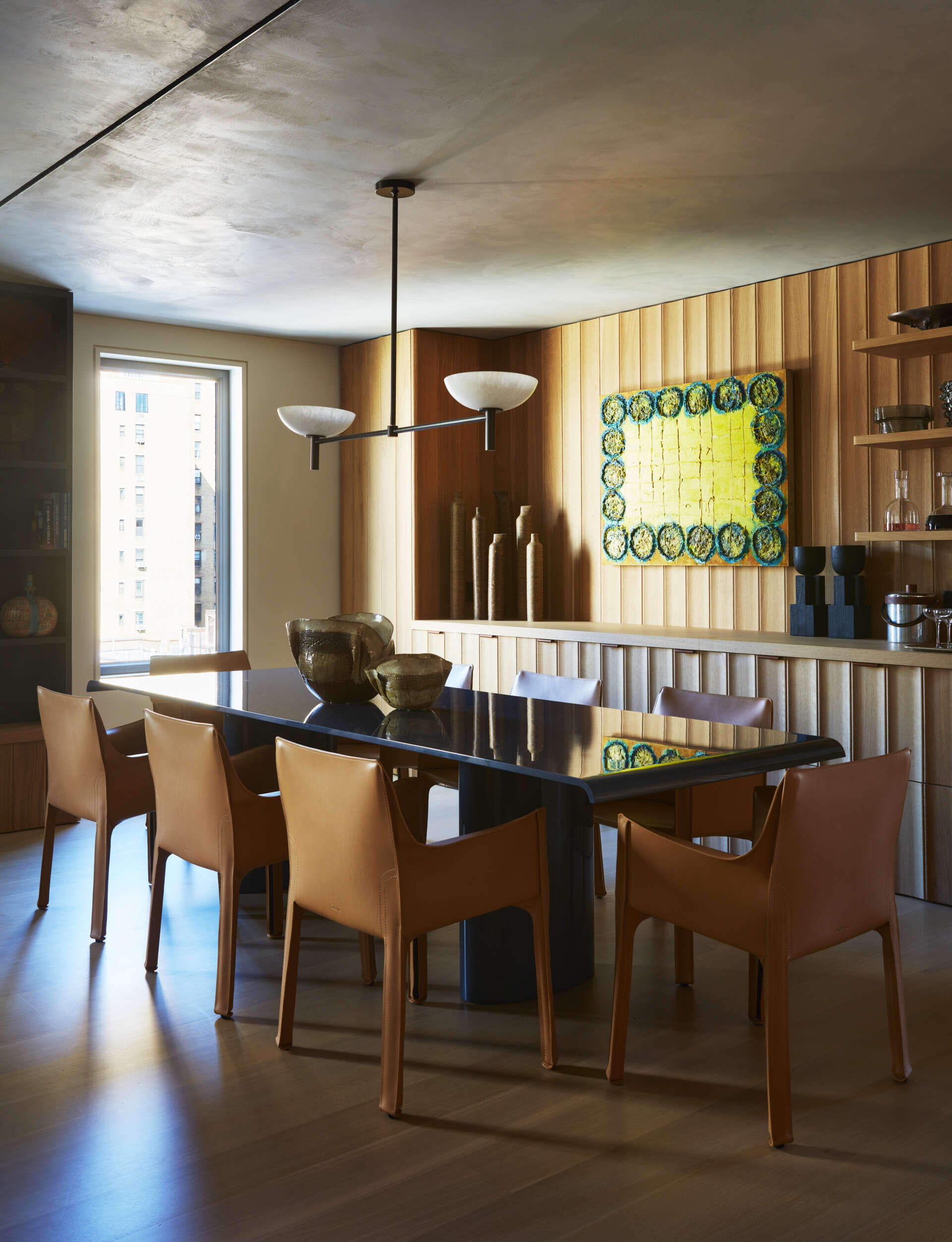 In the dining area, a dropped Venetian plaster ceiling introduces contrast and creates a more intimate atmosphere within the larger space. A custom lacquered dining table by MK Workshop sits beneath the sculptural Prato Pendant by Orphan Work, surrounded by Mario Bellini Cab chairs for Cassina.