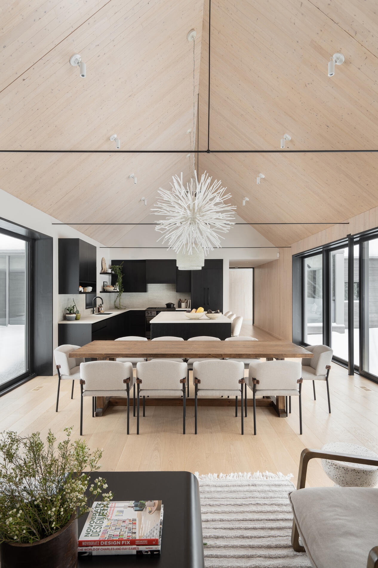 The dining area, with its large wood table and eye-catching light fixture, sits comfortably within the shared zone, maintaining a close relationship with both the living room and kitchen. 