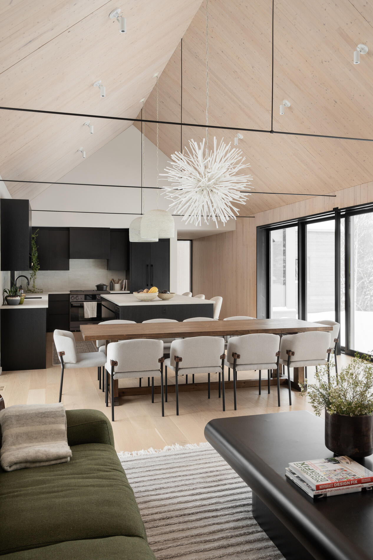 The dining area, with its large wood table and eye-catching light fixture, sits comfortably within the shared zone, maintaining a close relationship with both the living room and kitchen. 