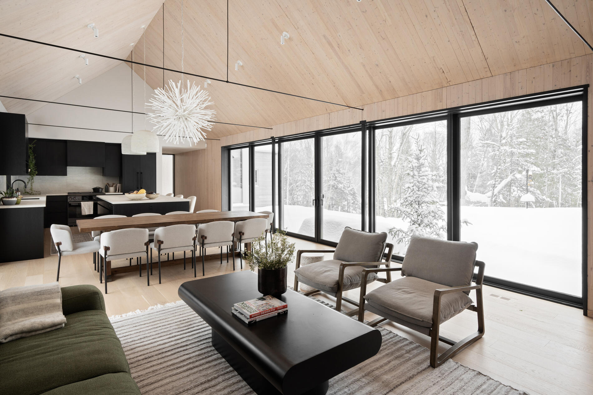The dining area, with its large wood table and eye-catching light fixture, sits comfortably within the shared zone, maintaining a close relationship with both the living room and kitchen. 