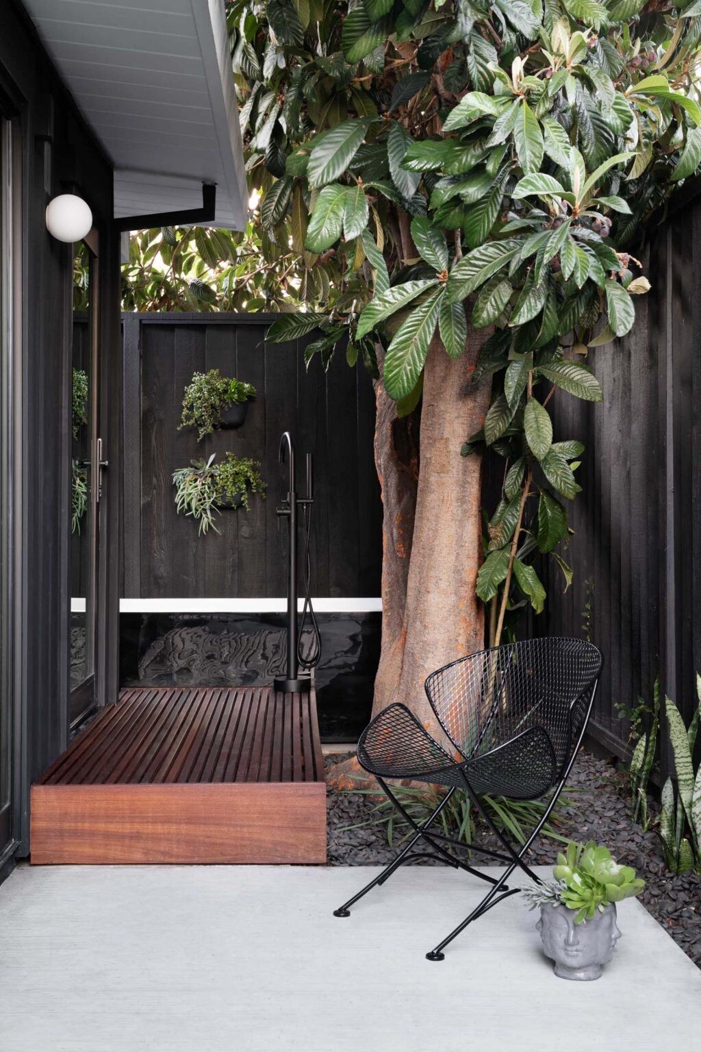 An indoor shower that opens to a private outdoor bathtub courtyard in a San Jose Eichler home, surrounded by fencing and planting for privacy and atmosphere.