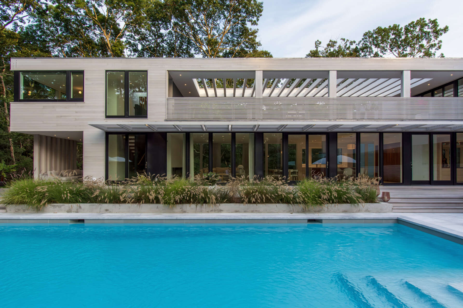A private pool terrace framed by cedar screens and trees creates an inviting outdoor space for summer living.