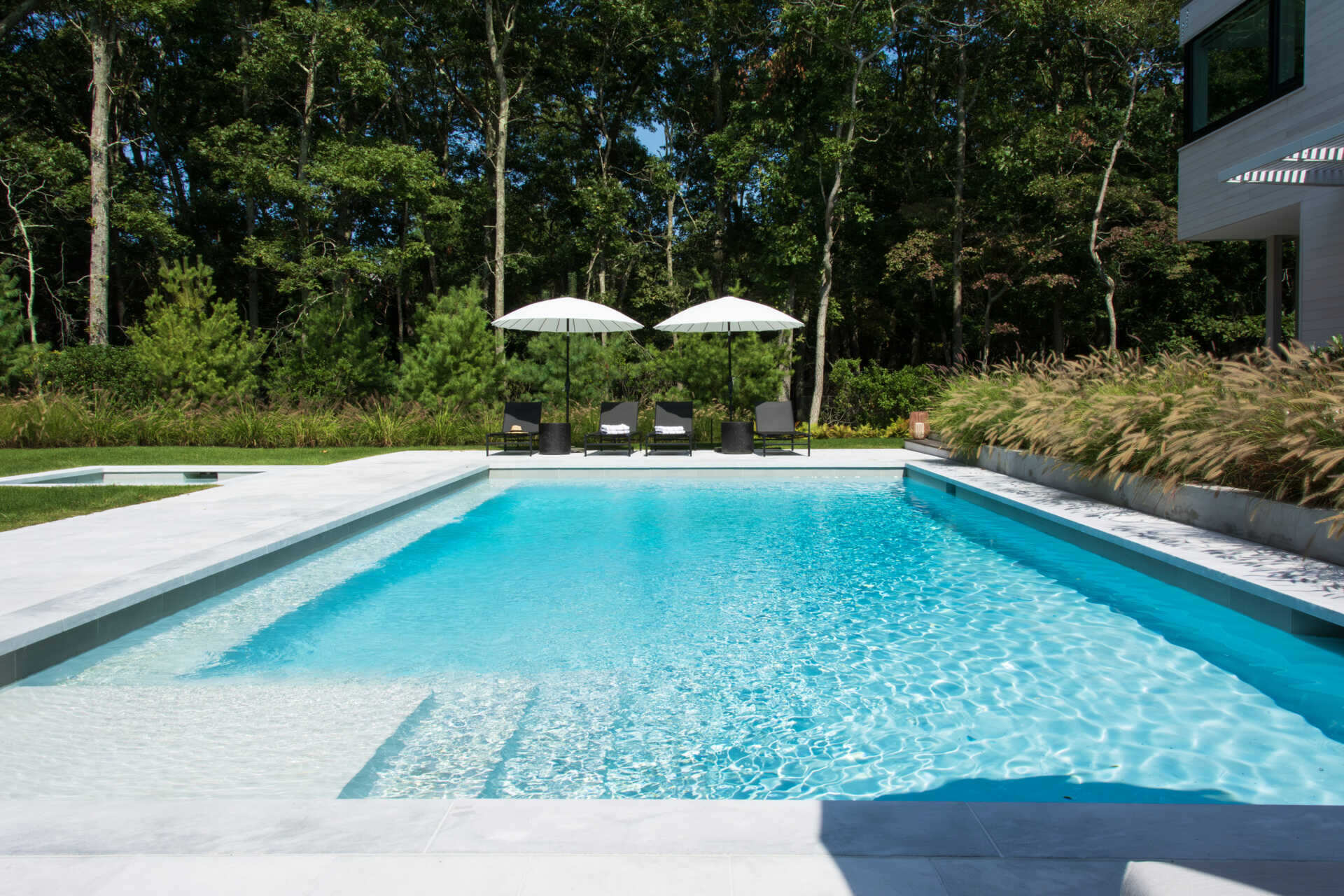 A private pool terrace framed by cedar screens and trees creates an inviting outdoor space for summer living.