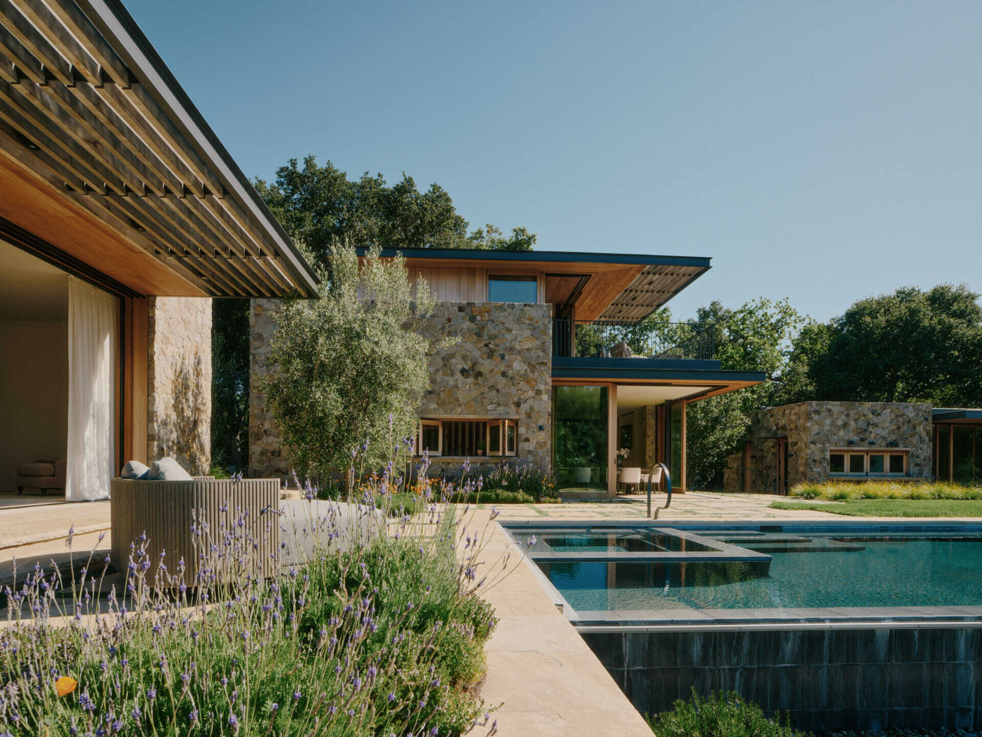 This ridge-top pool area combines stone walls, open views, and an outdoor shower for a relaxed California outdoor living experience.