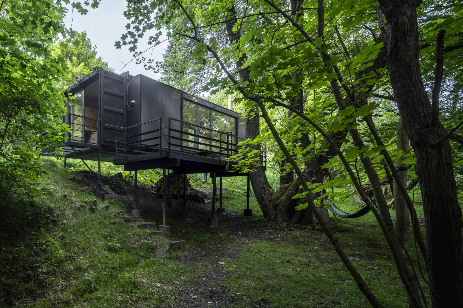 Offroadhouse in Wrzeszczyn, Poland transforms a recycled shipping container into a minimalist forest cabin with a raw industrial exterior, large deck, and peaceful natural setting beside water and dense vegetation.