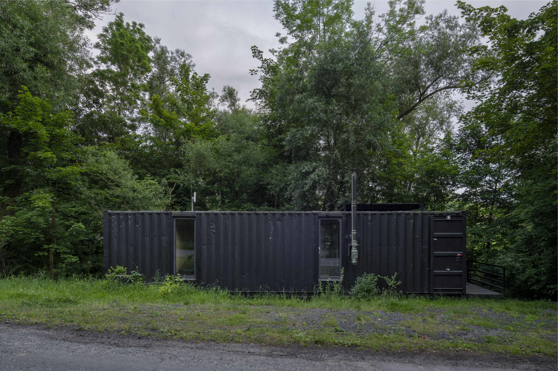 Offroadhouse in Wrzeszczyn, Poland transforms a recycled shipping container into a minimalist forest cabin with a raw industrial exterior, large deck, and peaceful natural setting beside water and dense vegetation.