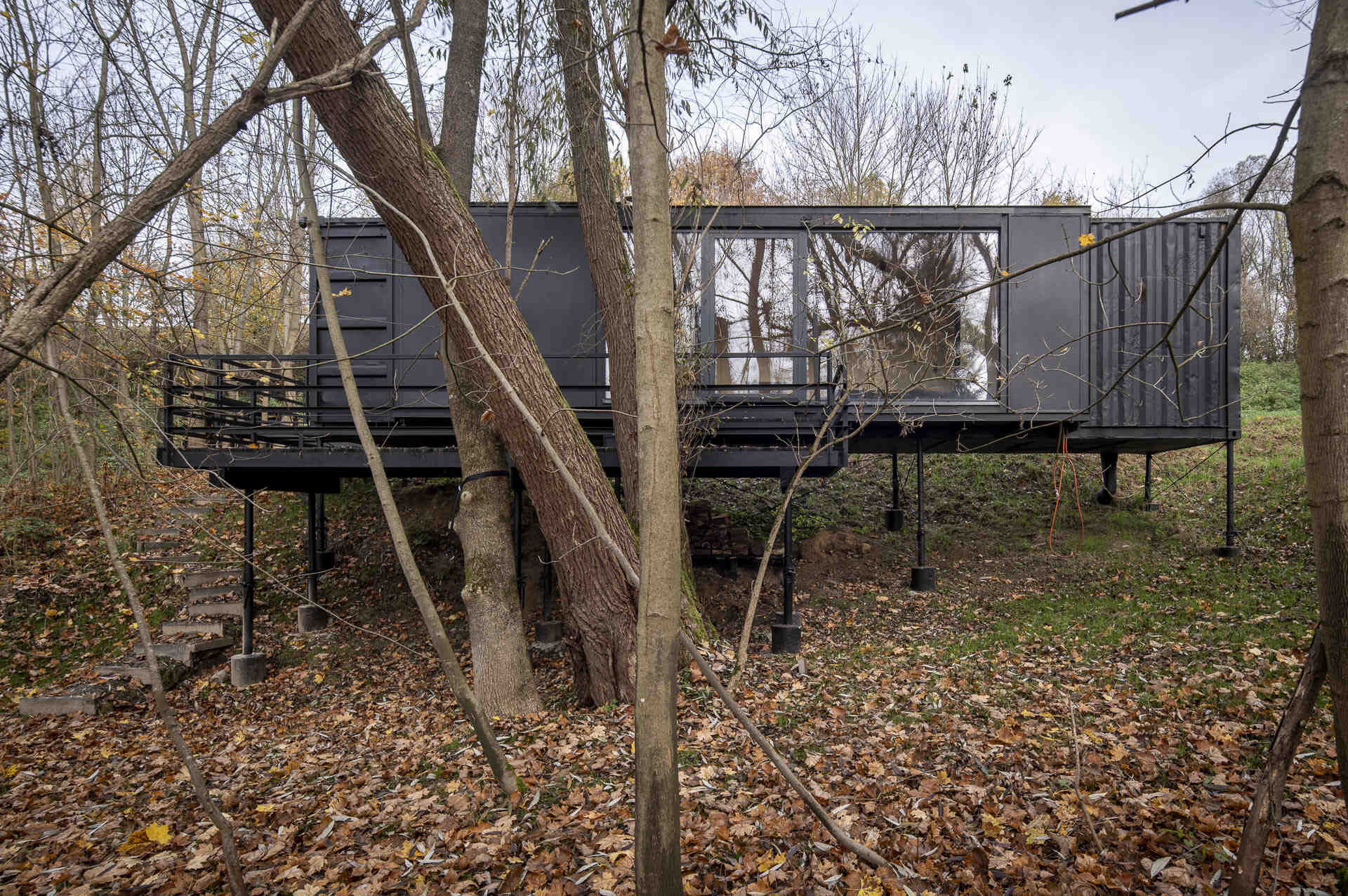 Offroadhouse in Wrzeszczyn, Poland transforms a recycled shipping container into a minimalist forest cabin with a raw industrial exterior, large deck, and peaceful natural setting beside water and dense vegetation.