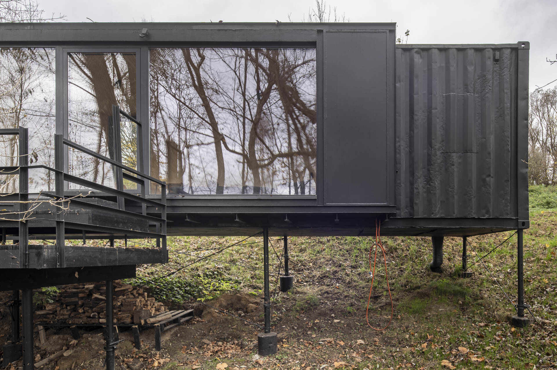 Offroadhouse in Wrzeszczyn, Poland transforms a recycled shipping container into a minimalist forest cabin with a raw industrial exterior, large deck, and peaceful natural setting beside water and dense vegetation.