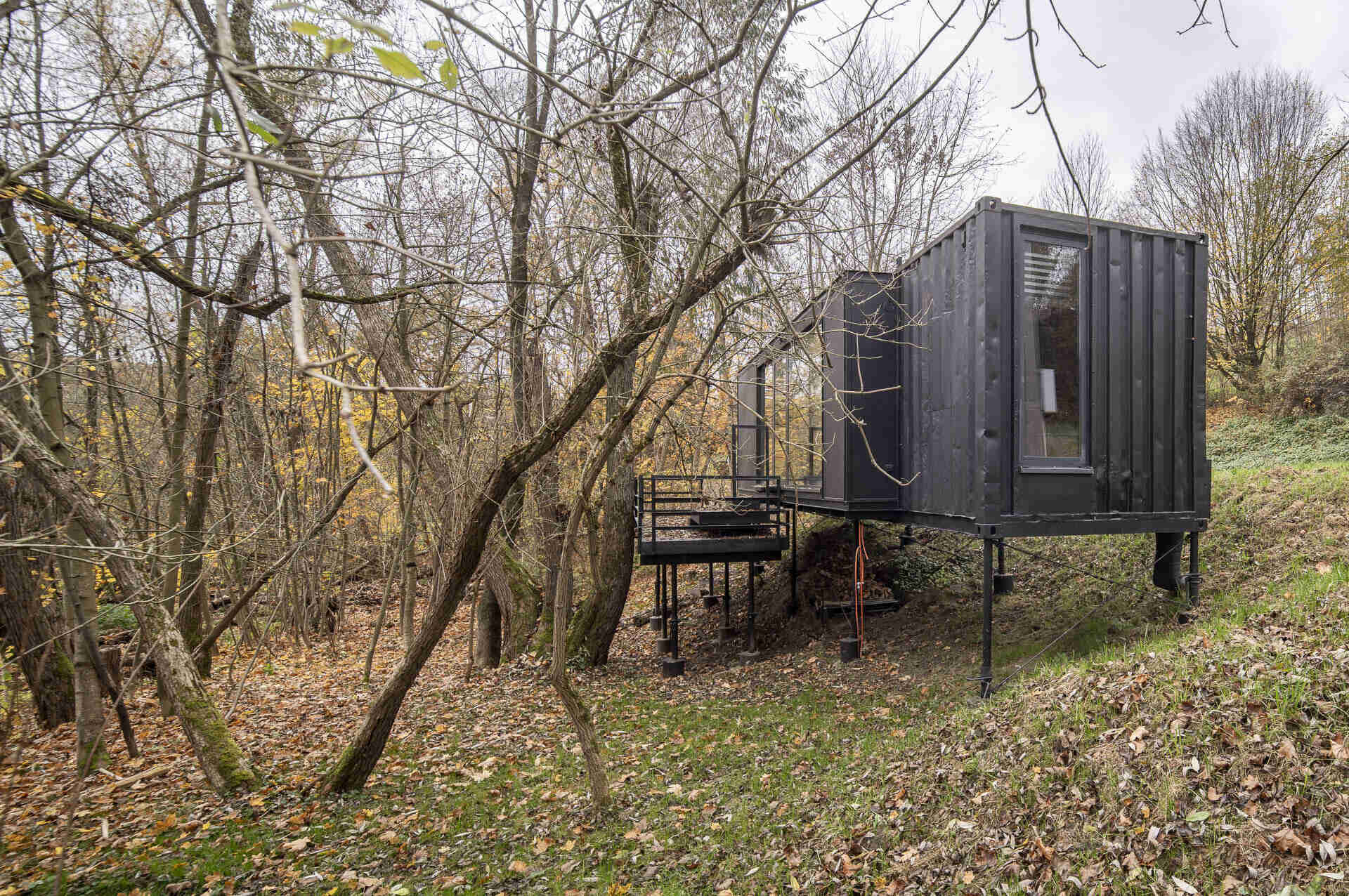Offroadhouse in Wrzeszczyn, Poland transforms a recycled shipping container into a minimalist forest cabin with a raw industrial exterior, large deck, and peaceful natural setting beside water and dense vegetation.