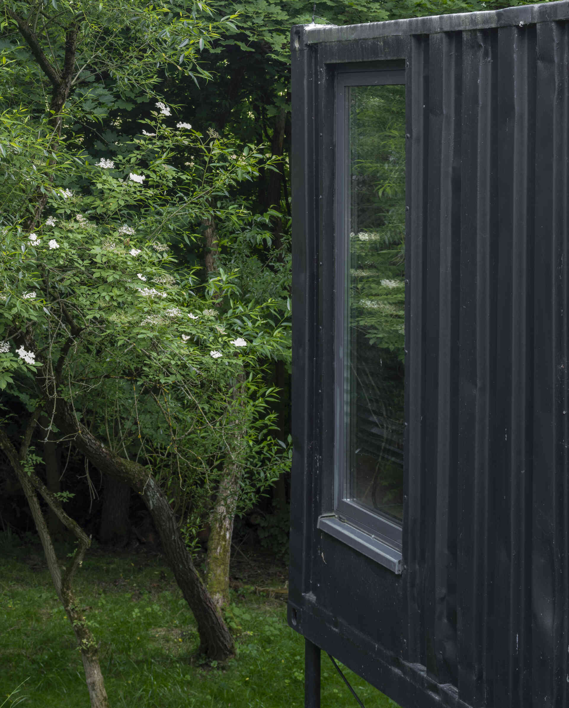 Offroadhouse in Wrzeszczyn, Poland transforms a recycled shipping container into a minimalist forest cabin with a raw industrial exterior, large deck, and peaceful natural setting beside water and dense vegetation.