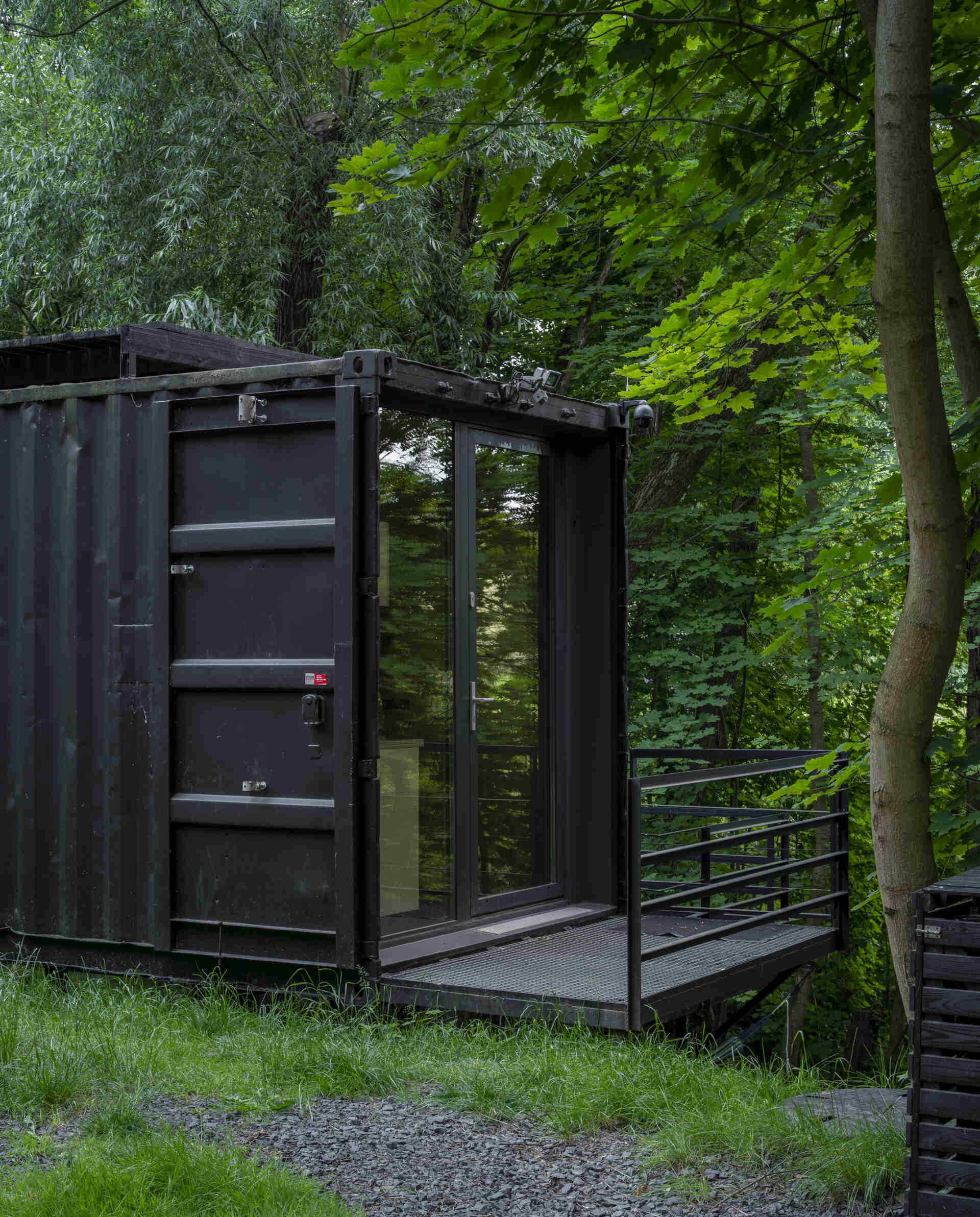 Offroadhouse in Wrzeszczyn, Poland transforms a recycled shipping container into a minimalist forest cabin with a raw industrial exterior, large deck, and peaceful natural setting beside water and dense vegetation.