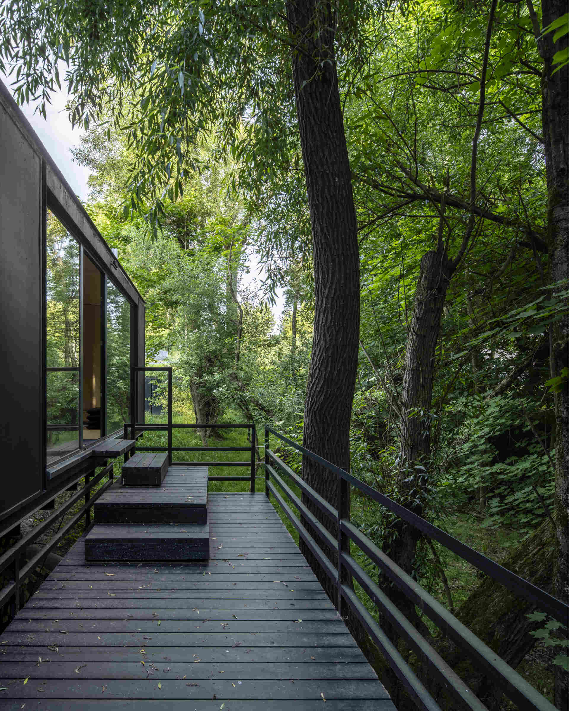 Offroadhouse in Wrzeszczyn, Poland transforms a recycled shipping container into a minimalist forest cabin with a raw industrial exterior, large deck, and peaceful natural setting beside water and dense vegetation.