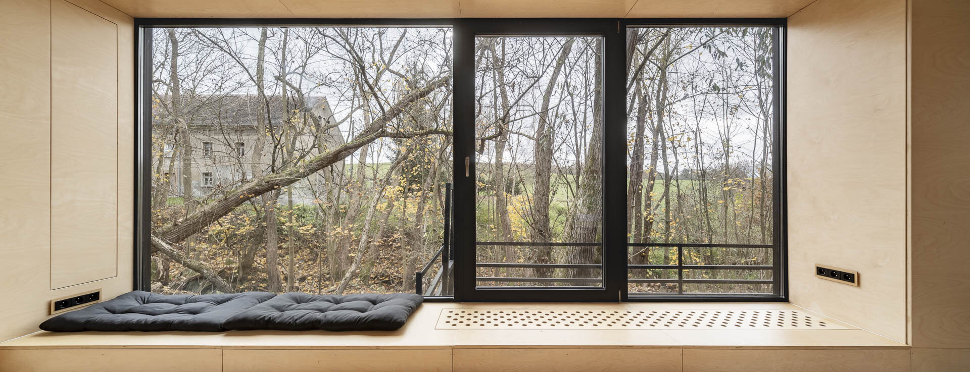 Inside Offroadhouse, warm plywood walls, hidden storage, a compact open-plan layout, and framed nature views create a calm minimalist interior inspired by Zen design.