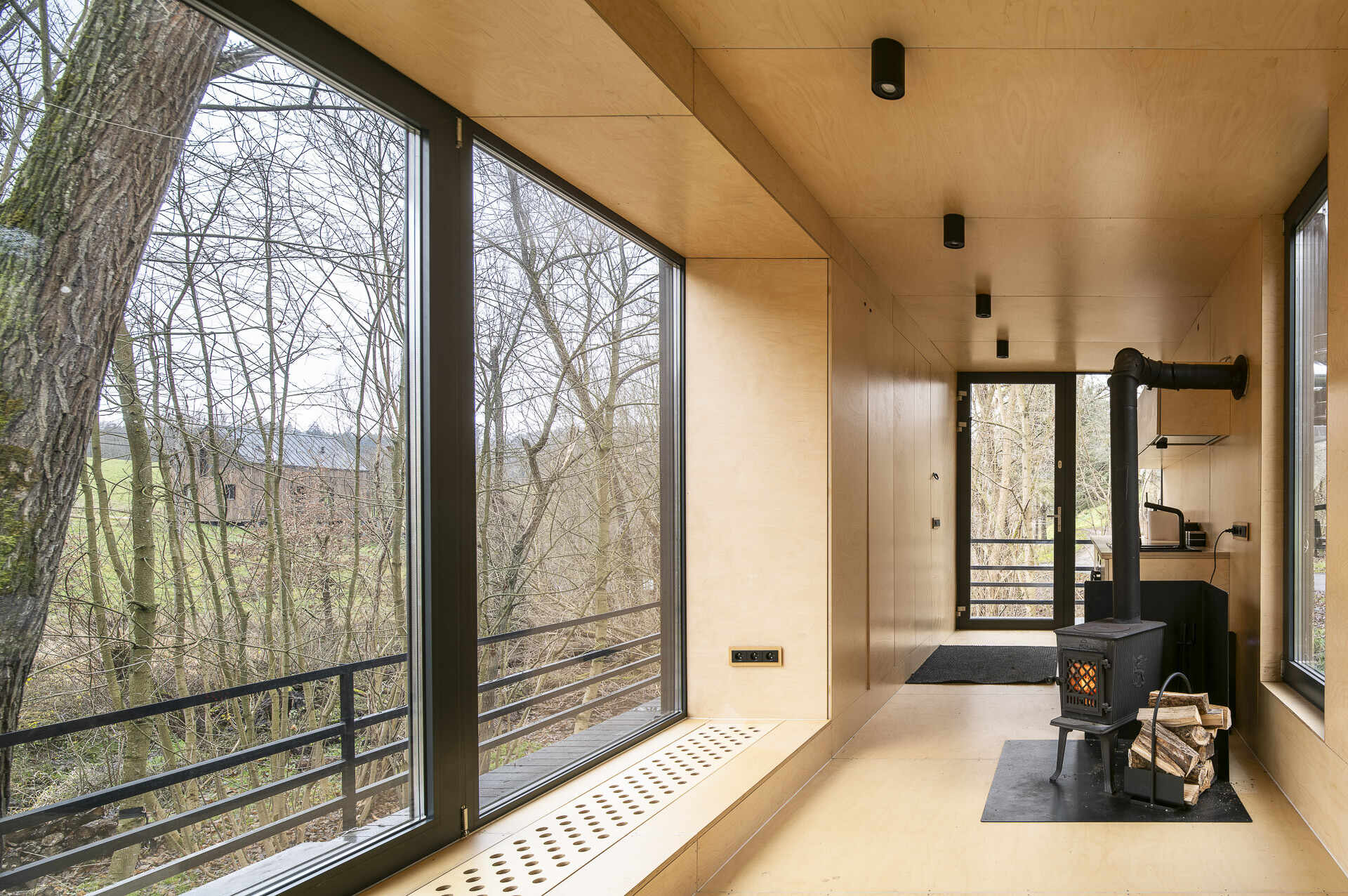 Inside Offroadhouse, warm plywood walls, hidden storage, a compact open-plan layout, and framed nature views create a calm minimalist interior inspired by Zen design.