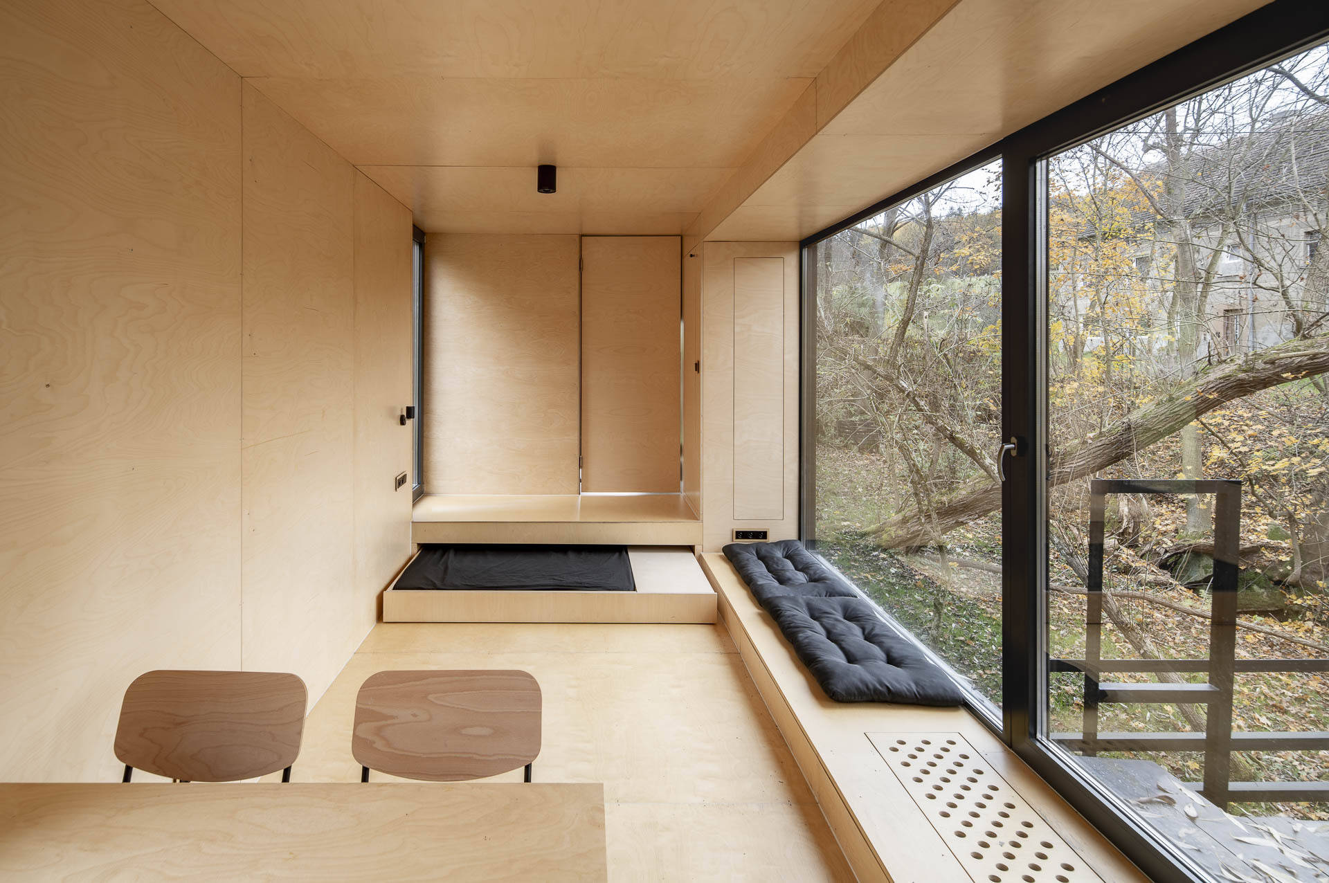 Inside Offroadhouse, warm plywood walls, hidden storage, a compact open-plan layout, and framed nature views create a calm minimalist interior inspired by Zen design.