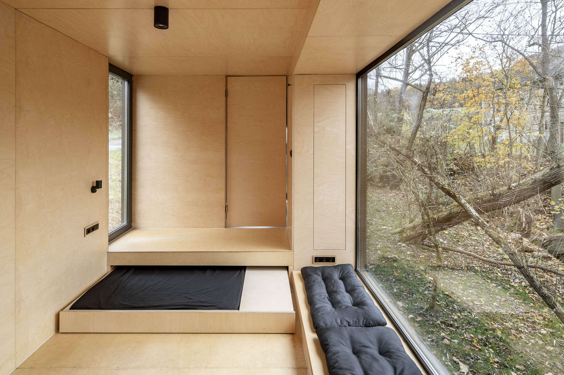 Inside Offroadhouse, warm plywood walls, hidden storage, a compact open-plan layout, and framed nature views create a calm minimalist interior inspired by Zen design.