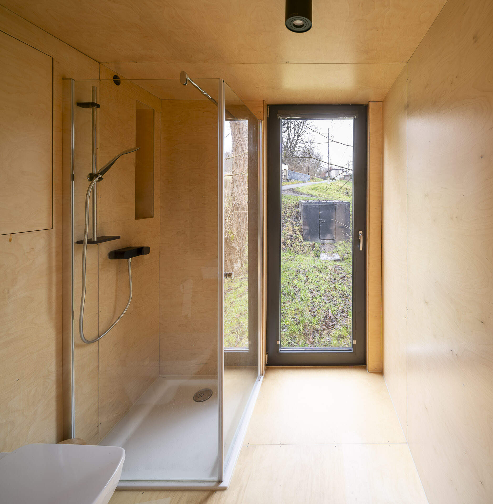 Inside Offroadhouse, warm plywood walls, hidden storage, a compact open-plan layout, and framed nature views create a calm minimalist interior inspired by Zen design.