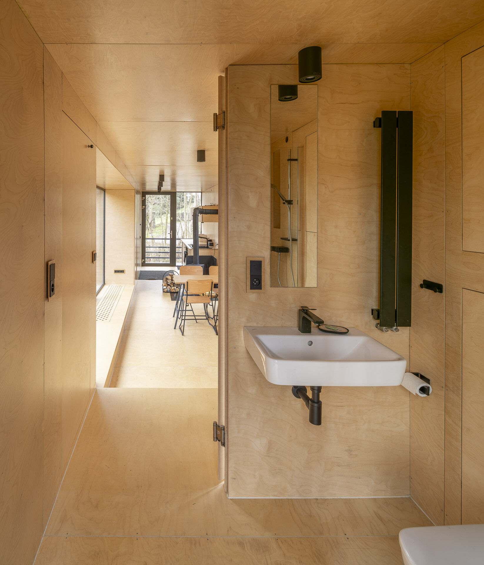 Inside Offroadhouse, warm plywood walls, hidden storage, a compact open-plan layout, and framed nature views create a calm minimalist interior inspired by Zen design.