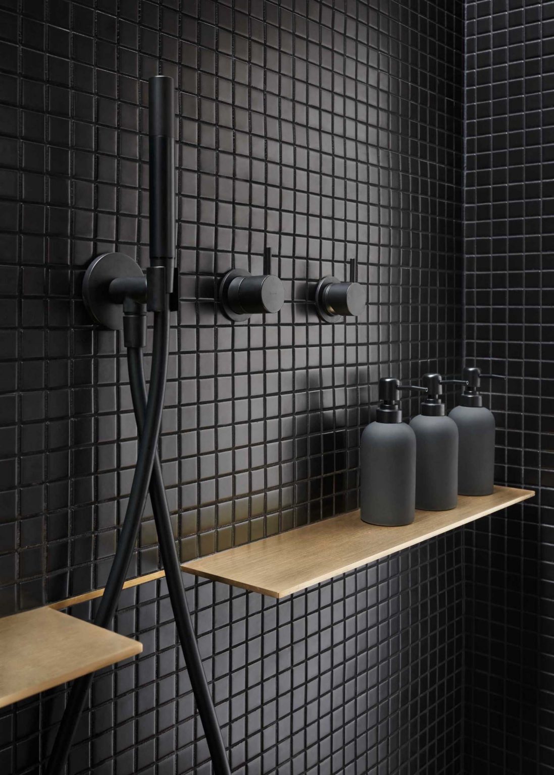 A black-on-black ensuite with mahogany cabinetry, brass accents, and matte black mosaic tiles creating a subtle, warm-toned bathroom interior in a San Jose Eichler home.