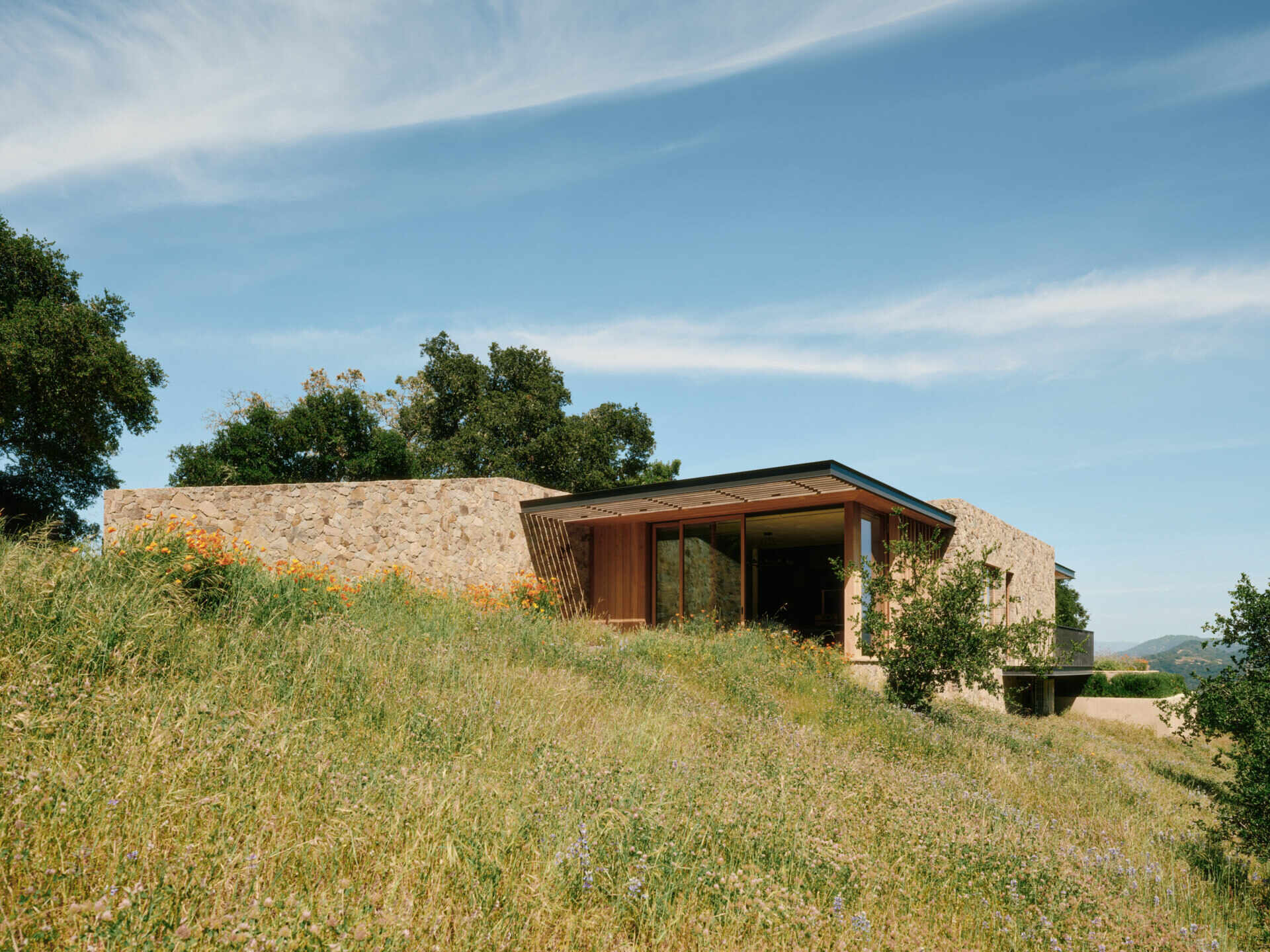 Four separate stone pavilions step across the California hillside, creating a modern villa layout inspired by Tuscan villages and open-air living.
