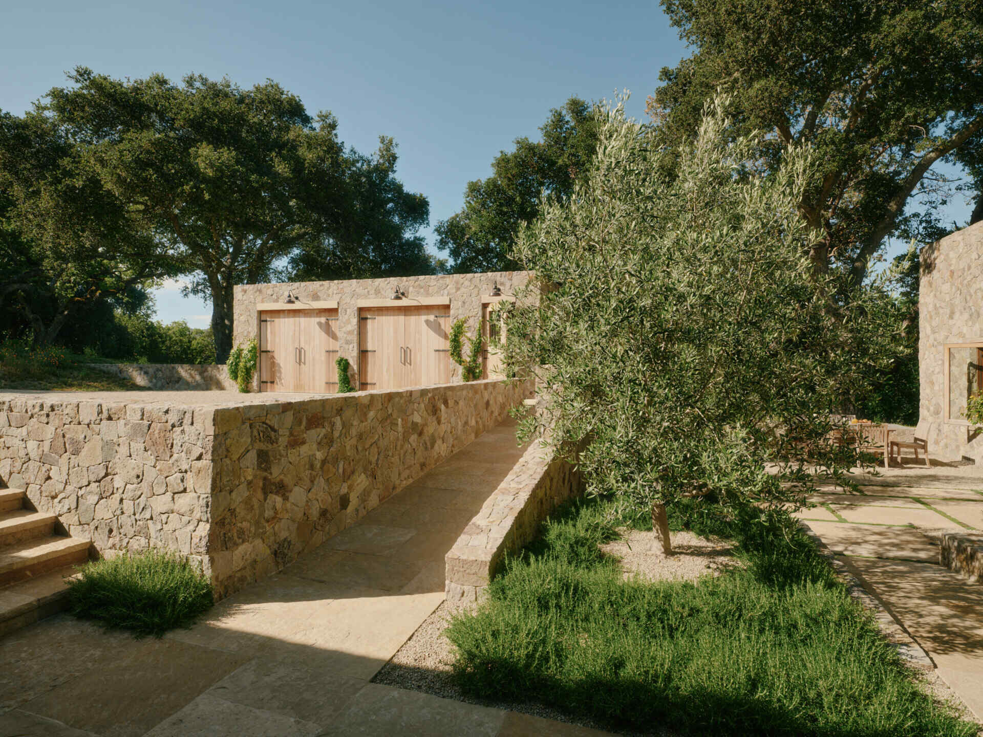 Four separate stone pavilions step across the California hillside, creating a modern villa layout inspired by Tuscan villages and open-air living.