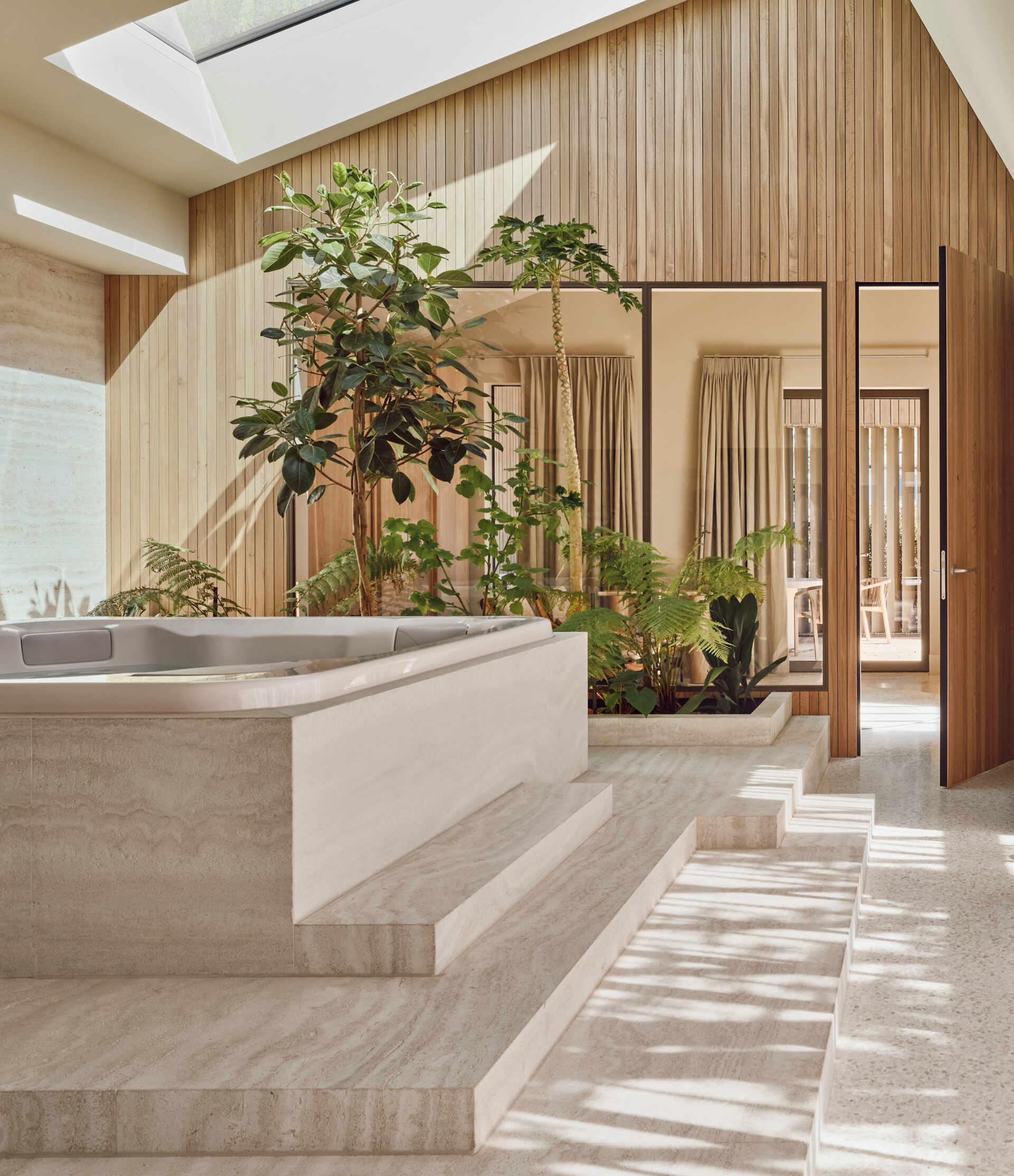 Travertine walls, a garden-facing jacuzzi, and sculptural lounge furniture turn this wellness wing into a luxurious escape at home.