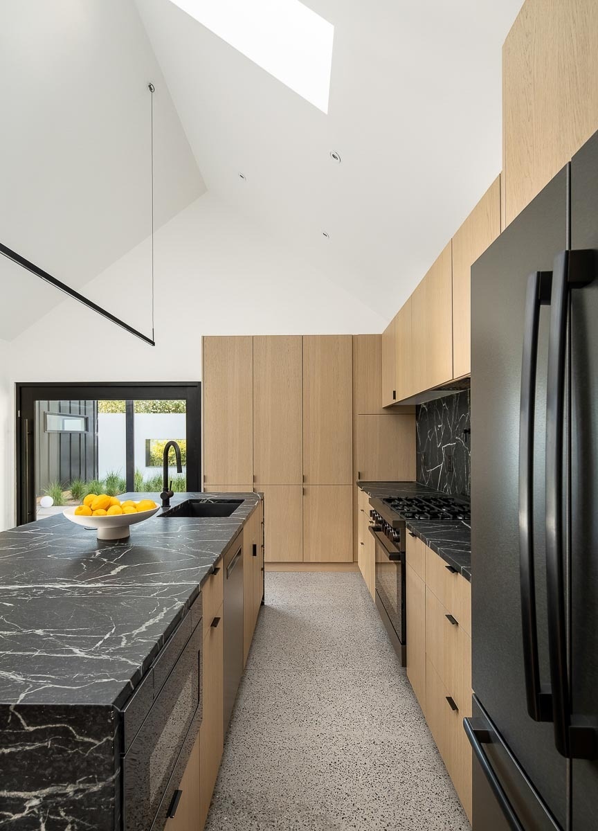 White oak cabinets, dark soapstone countertops, and black appliances create a warm modern kitchen inside this remodeled Phoenix house.