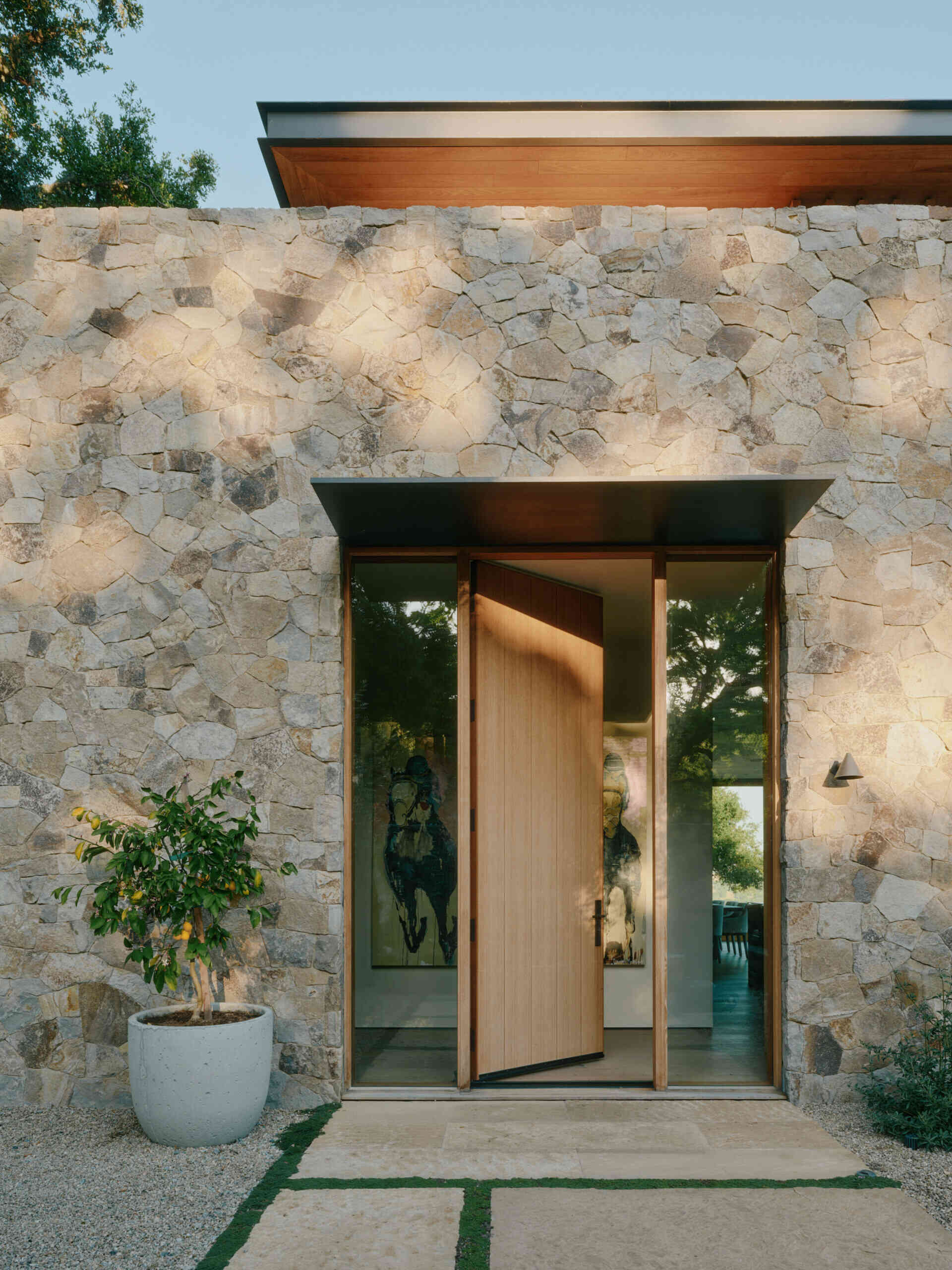 The entrance to Stone Villa uses textured stone walls, shaded openings, and layered pathways to create a warm modern arrival.