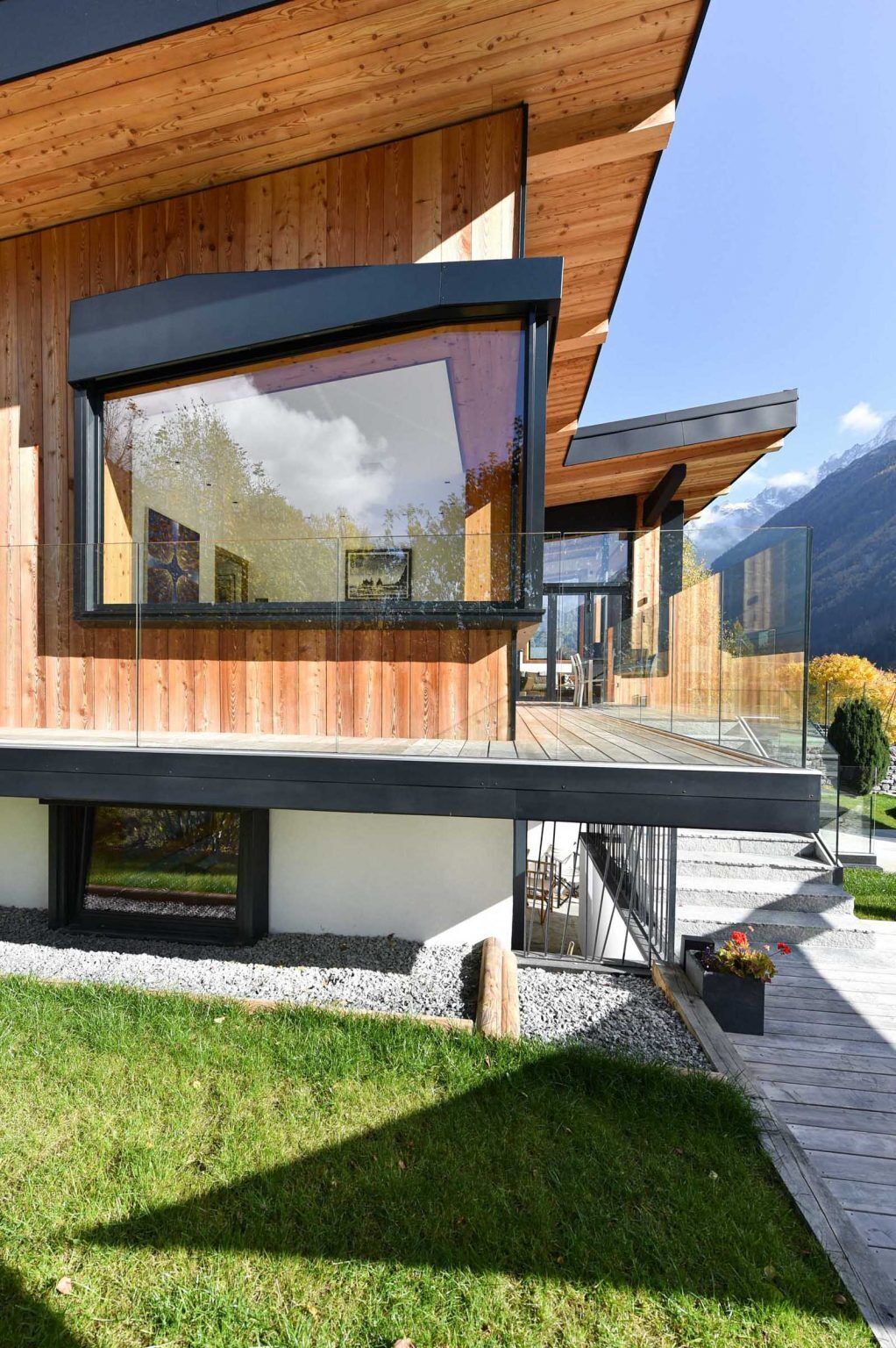 Glass railings, wood siding, and mountain views define the outdoor spaces of this modern alpine home in Chamonix, France.
