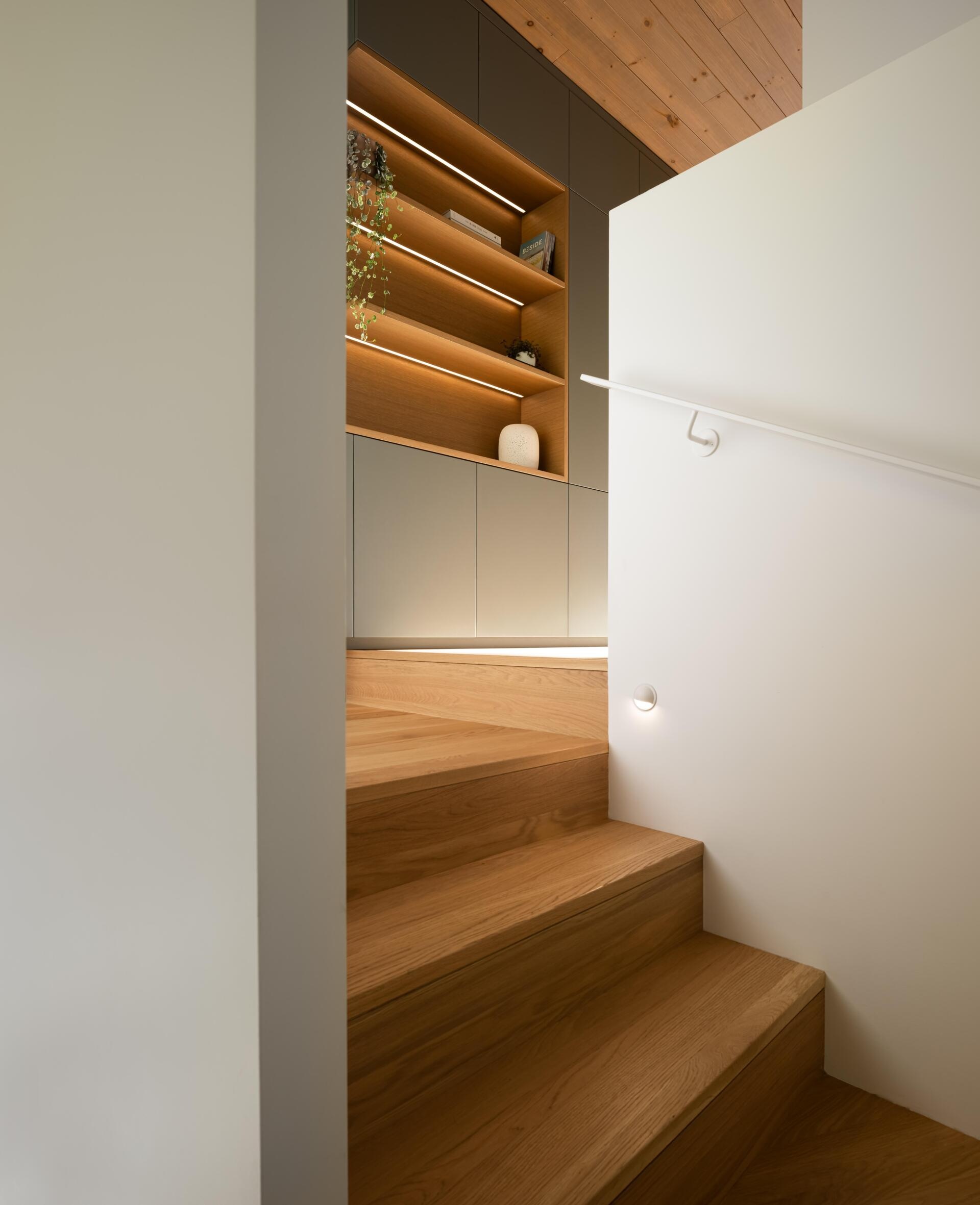 Wood stairs lead up to a primary suite with built-in storage and open shelving with hidden lighting.