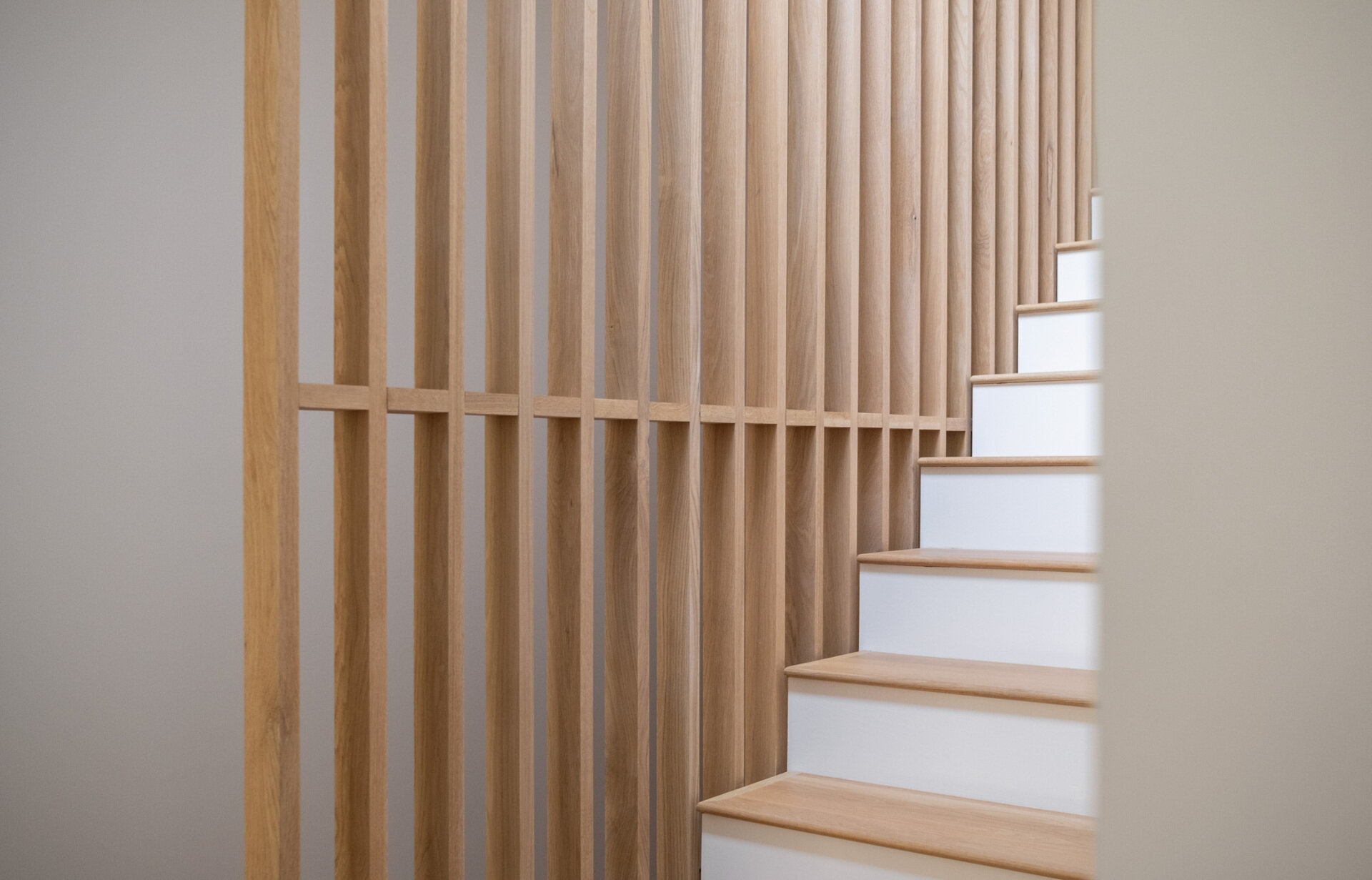 The wood and white staircase acts connects between levels, while natural light filtering through nearby glazing and the wood slat divider helps prevent the stair zone from feeling enclosed.