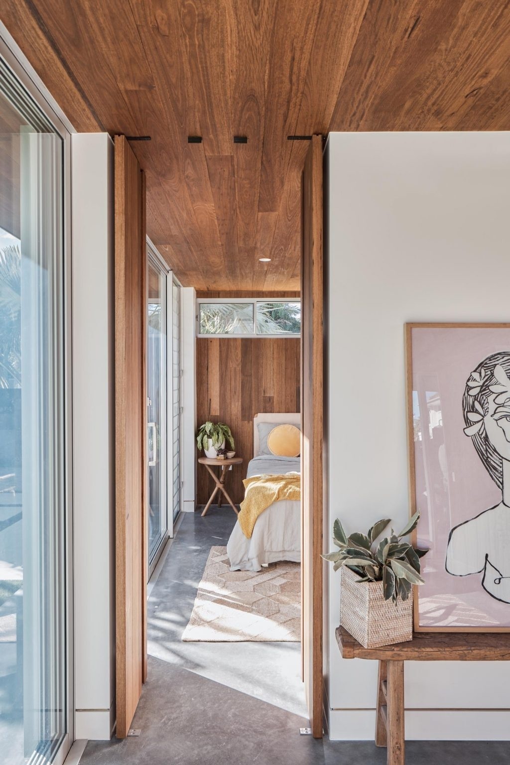 The bedroom in this Australian backyard studio features a continuous timber ceiling and wall detail that creates a warm modern backdrop for the bed.