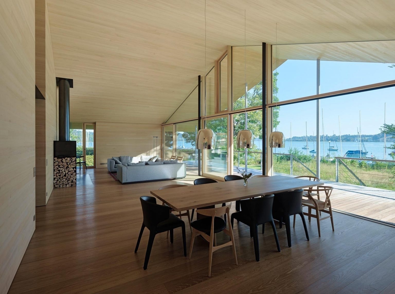 Floor-to-ceiling windows frame sweeping lake views inside the open-plan living and dining room of this timber home in Germany.