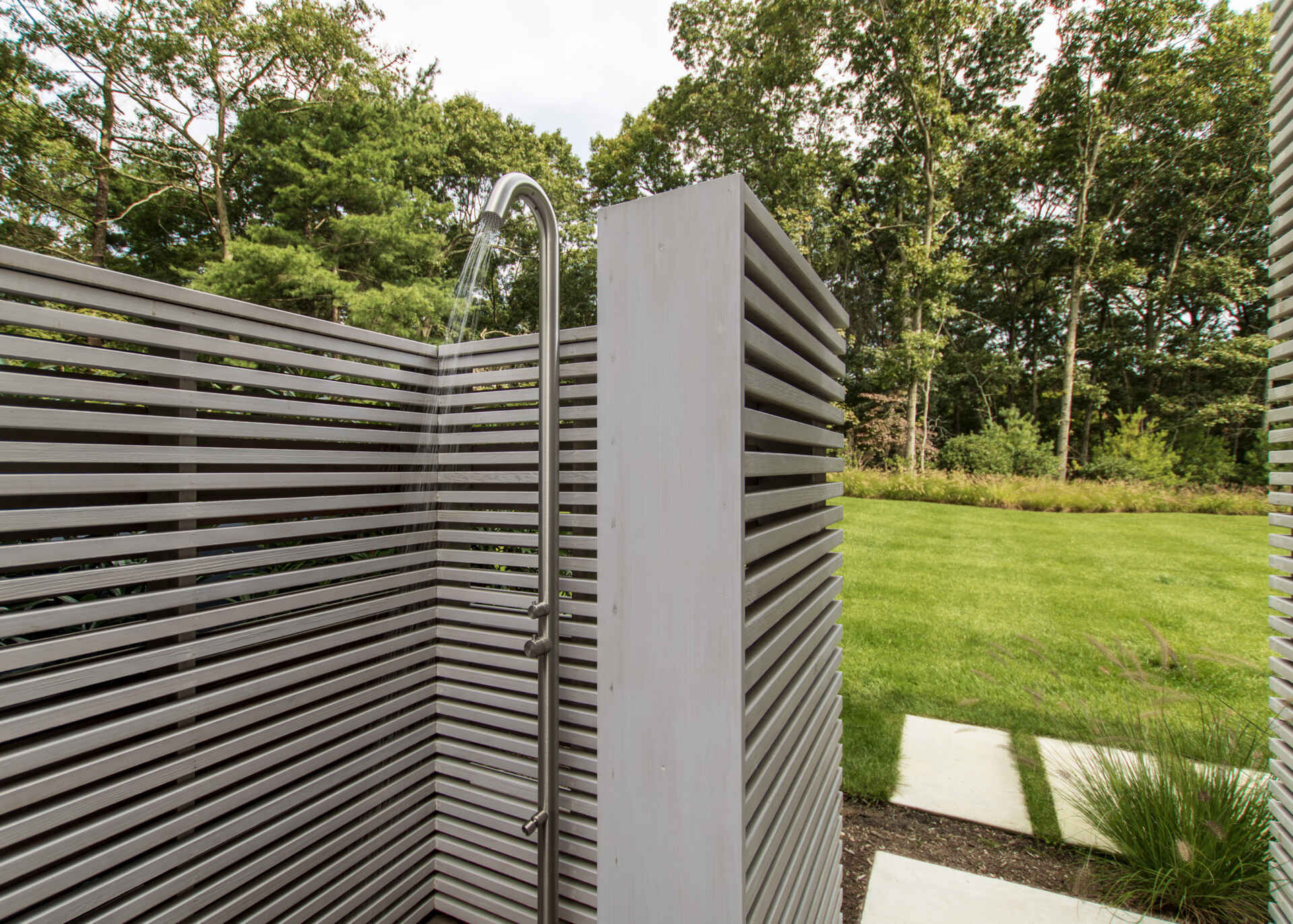 A private pool terrace framed by cedar screens and trees creates an inviting outdoor space for summer living.