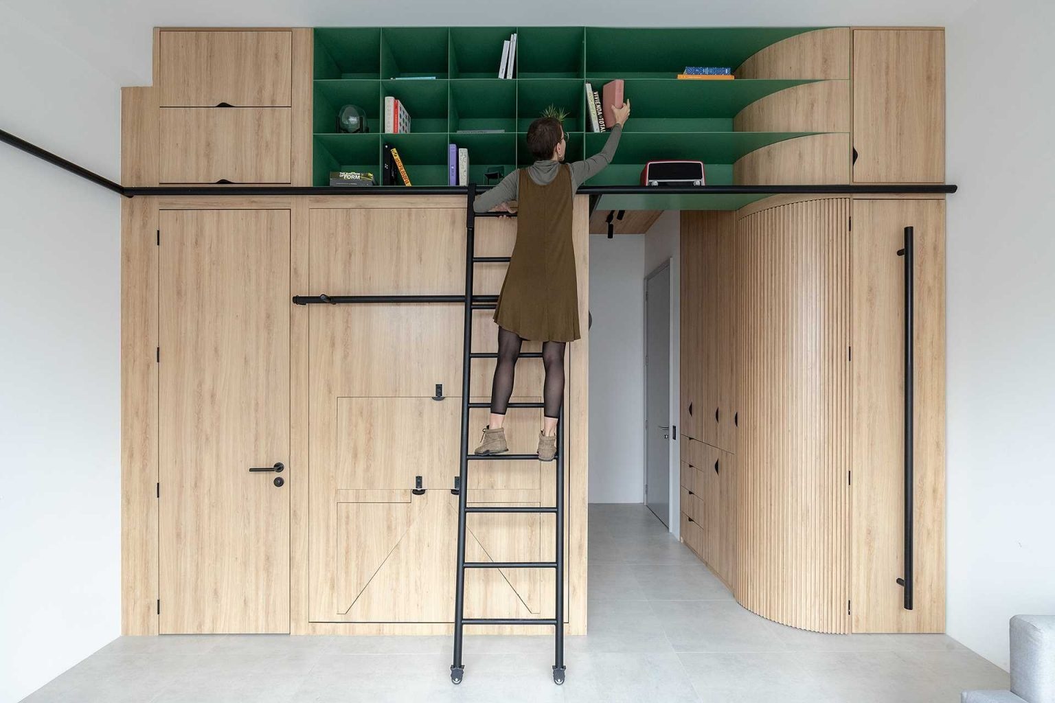 A black metal ladder provides access to ceiling-height storage, helping this compact apartment maximize every inch of available space.