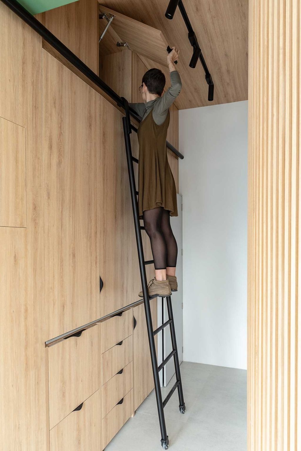 A black metal ladder provides access to ceiling-height storage, helping this compact apartment maximize every inch of available space.