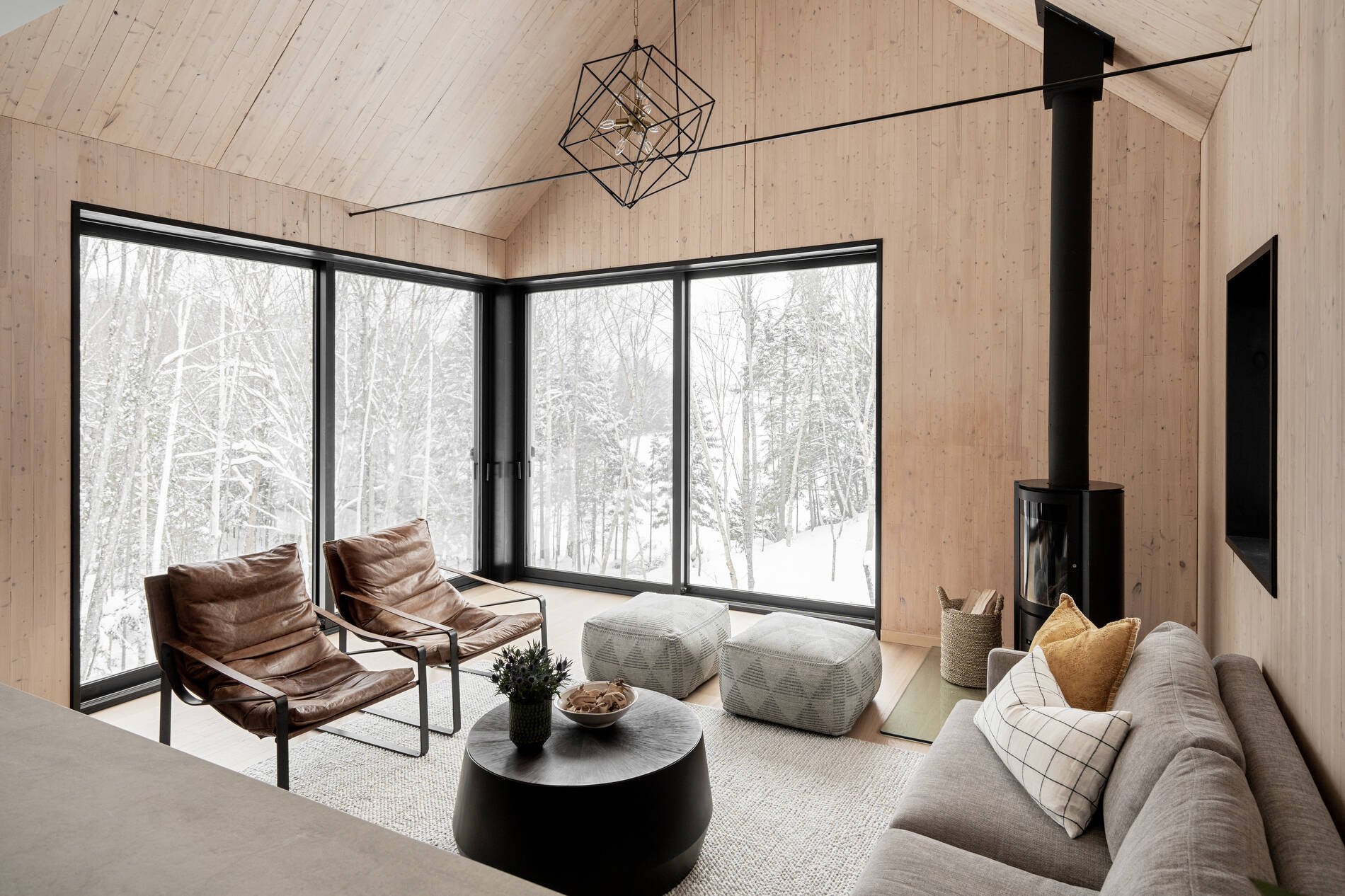 A modern living room with a fireplace in the corner and large windows that look out onto the landscape.