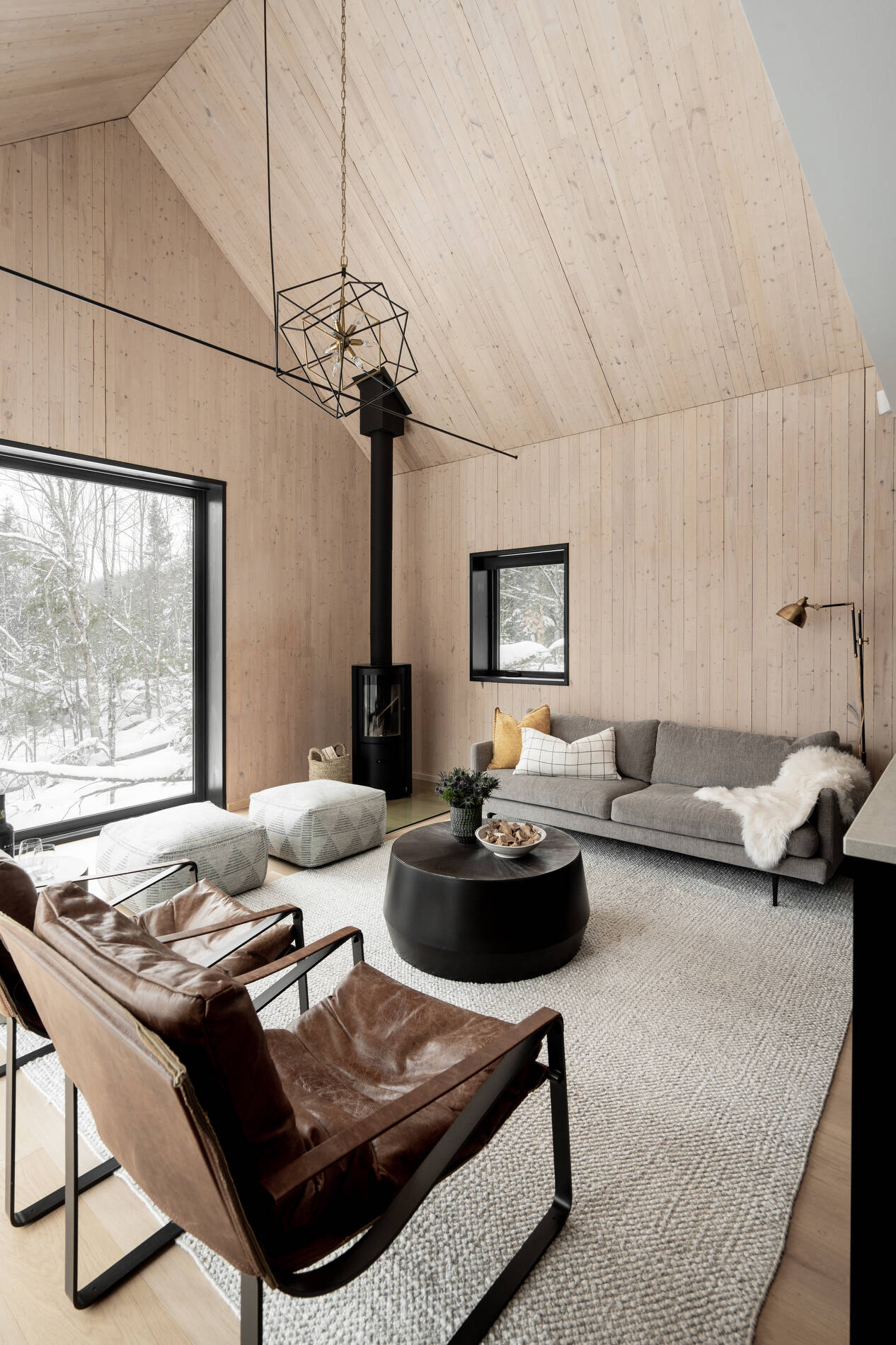 A modern living room with a fireplace in the corner and large windows that look out onto the landscape.