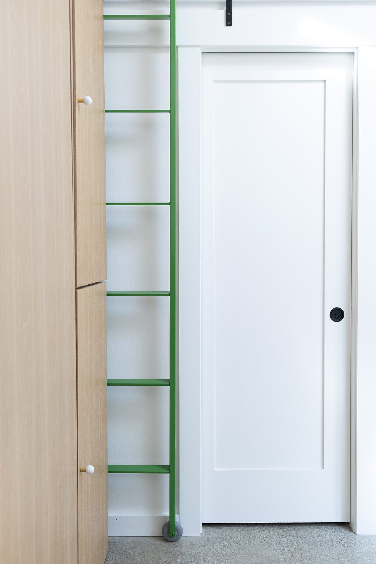 A bright green rolling ladder leads to a loft storage area, adding functionality and personality to this compact backyard studio.