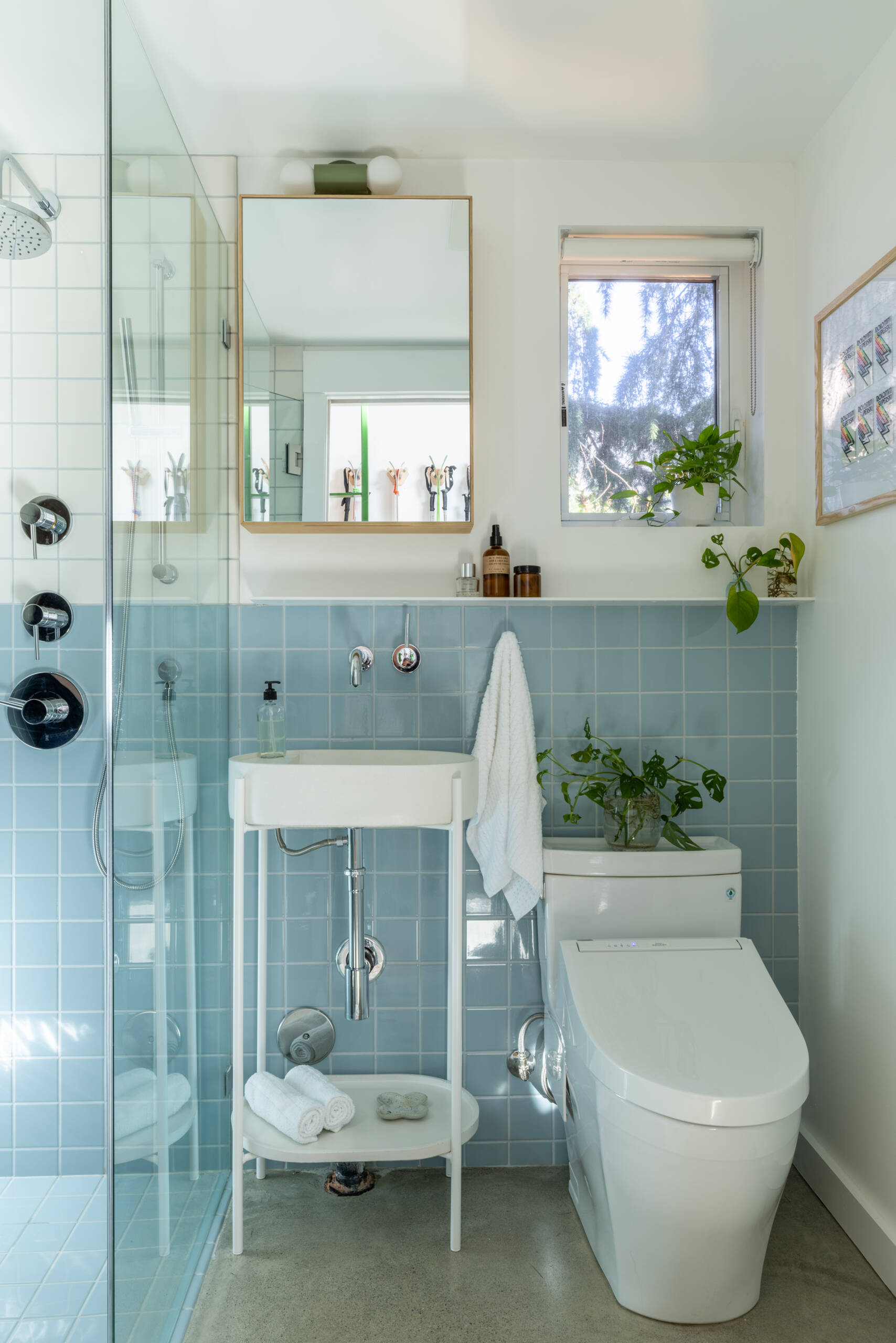 This compact bathroom combines blue tile, a concrete sink, floating shelves, and a barrier-free shower to create a bright and spacious feel.