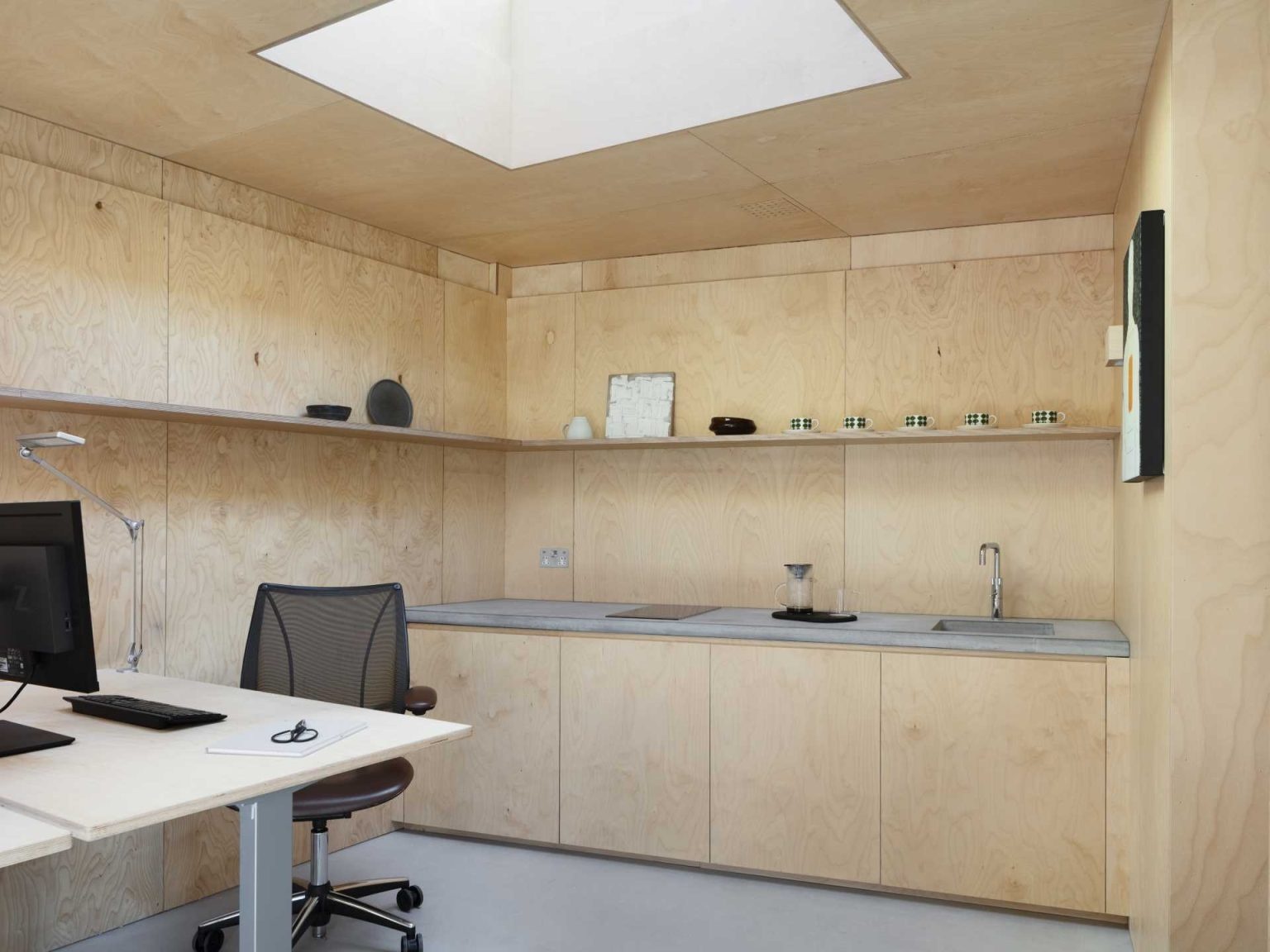 A simple kitchenette, a skylight, and continuous shelving help maximize light and storage in this small studio office.