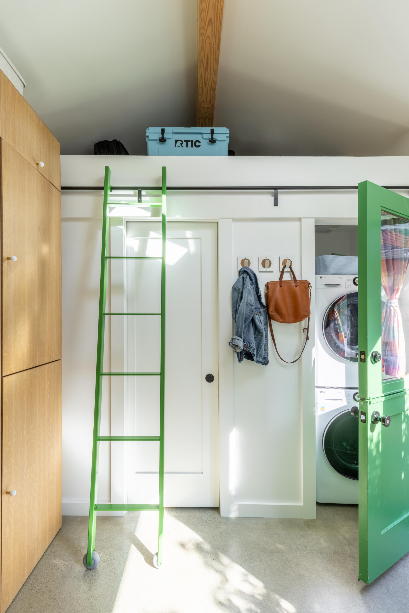 A bright green rolling ladder leads to a loft storage area, adding functionality and personality to this compact backyard studio.
