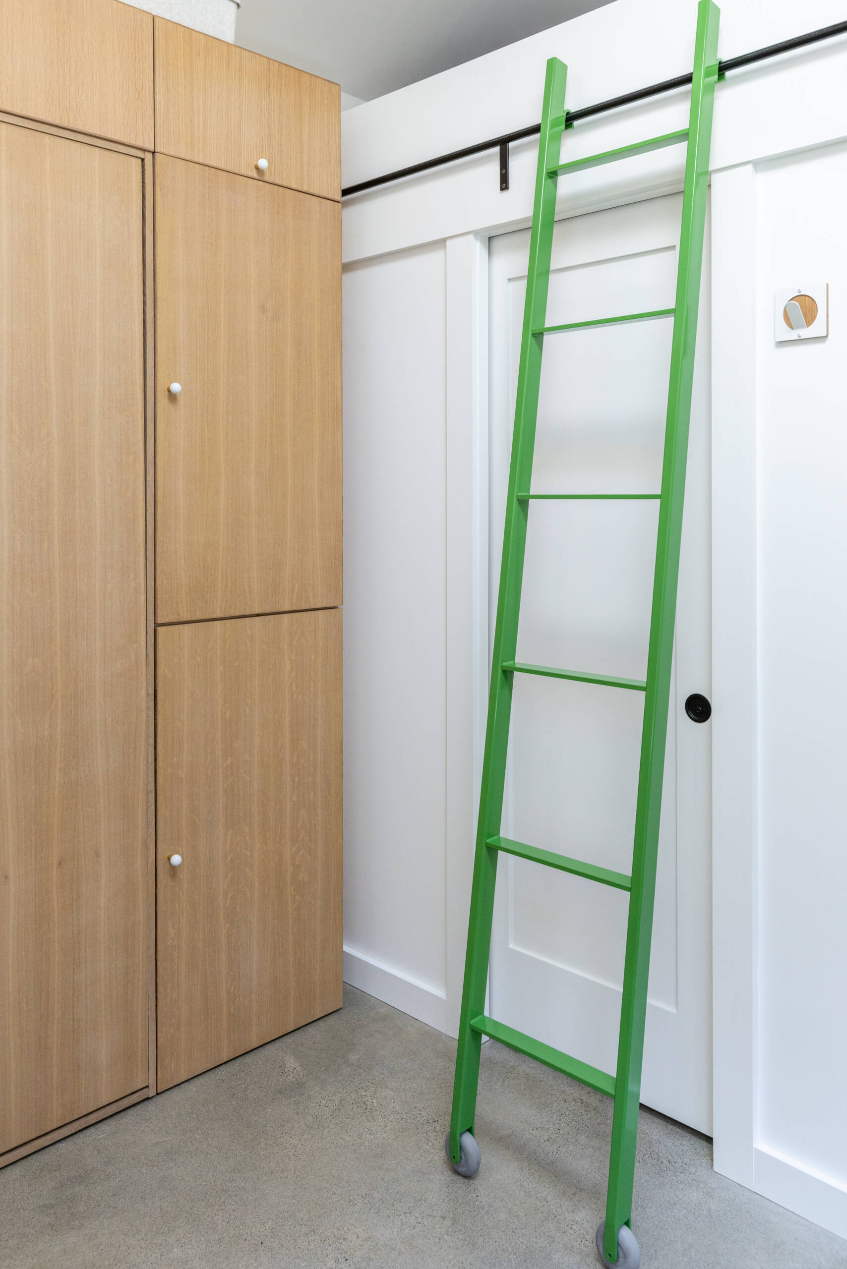 A bright green rolling ladder leads to a loft storage area, adding functionality and personality to this compact backyard studio.