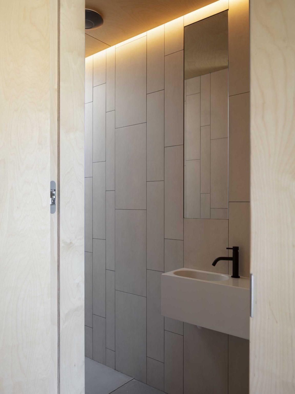 Tiled walls, a tall mirror, and concealed lighting make this compact bathroom feel brighter and more spacious.