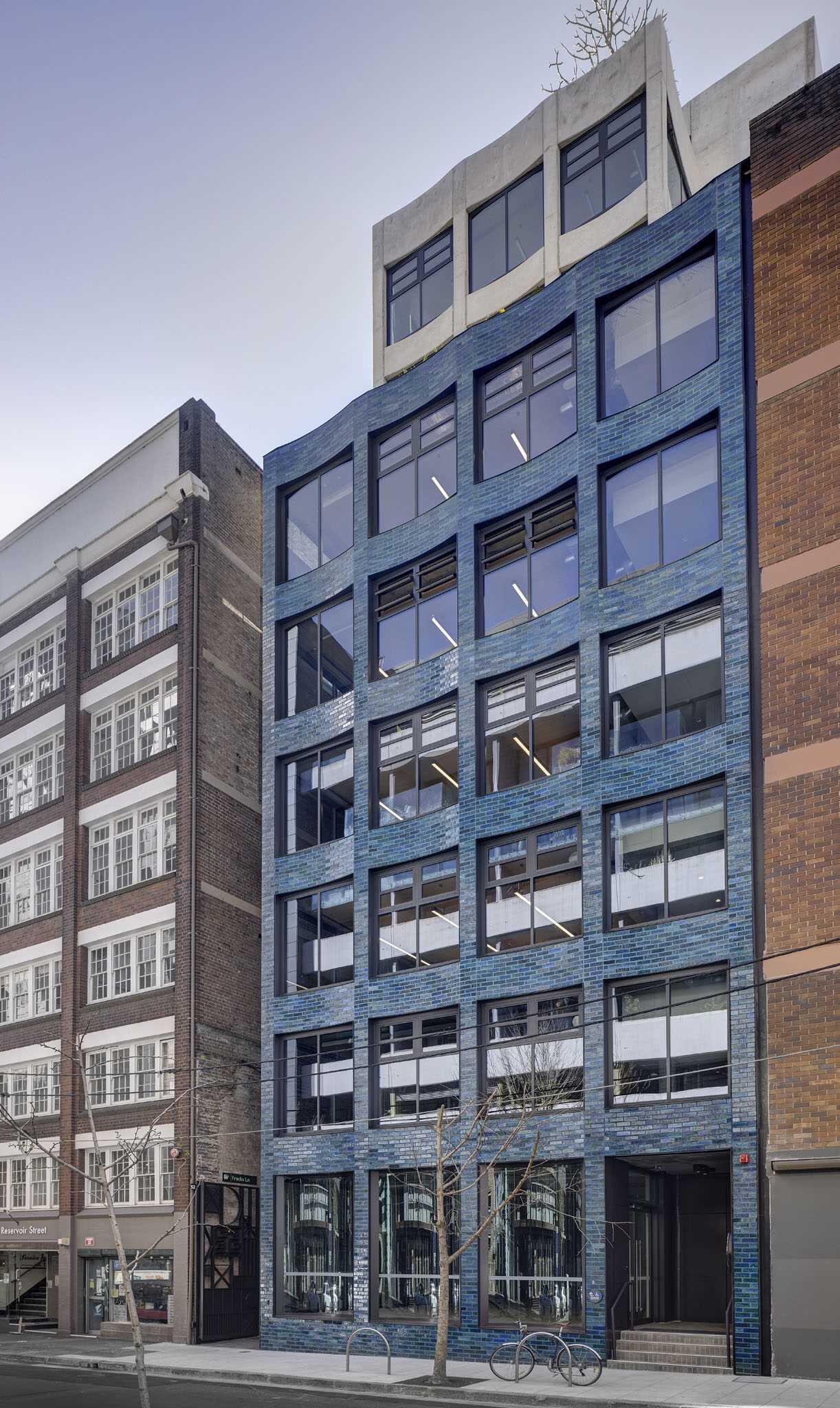 This aquamarine glazed-brick facade by SJB turns a Sydney office building into a sculptural landmark filled with texture, color, and architectural detail.