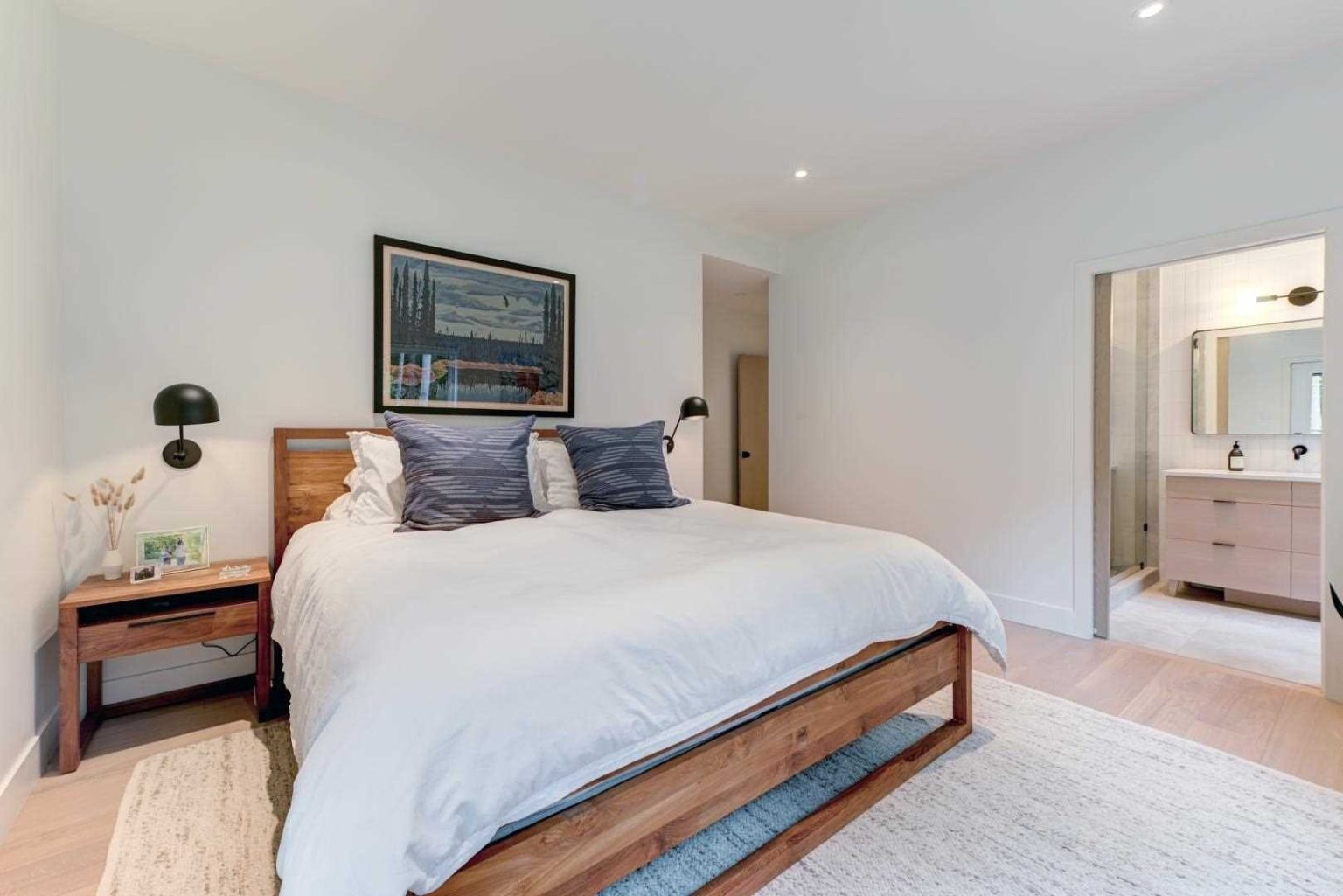 Minimal decor, black sconces, and subtle artwork create a serene and stylish main bedroom.